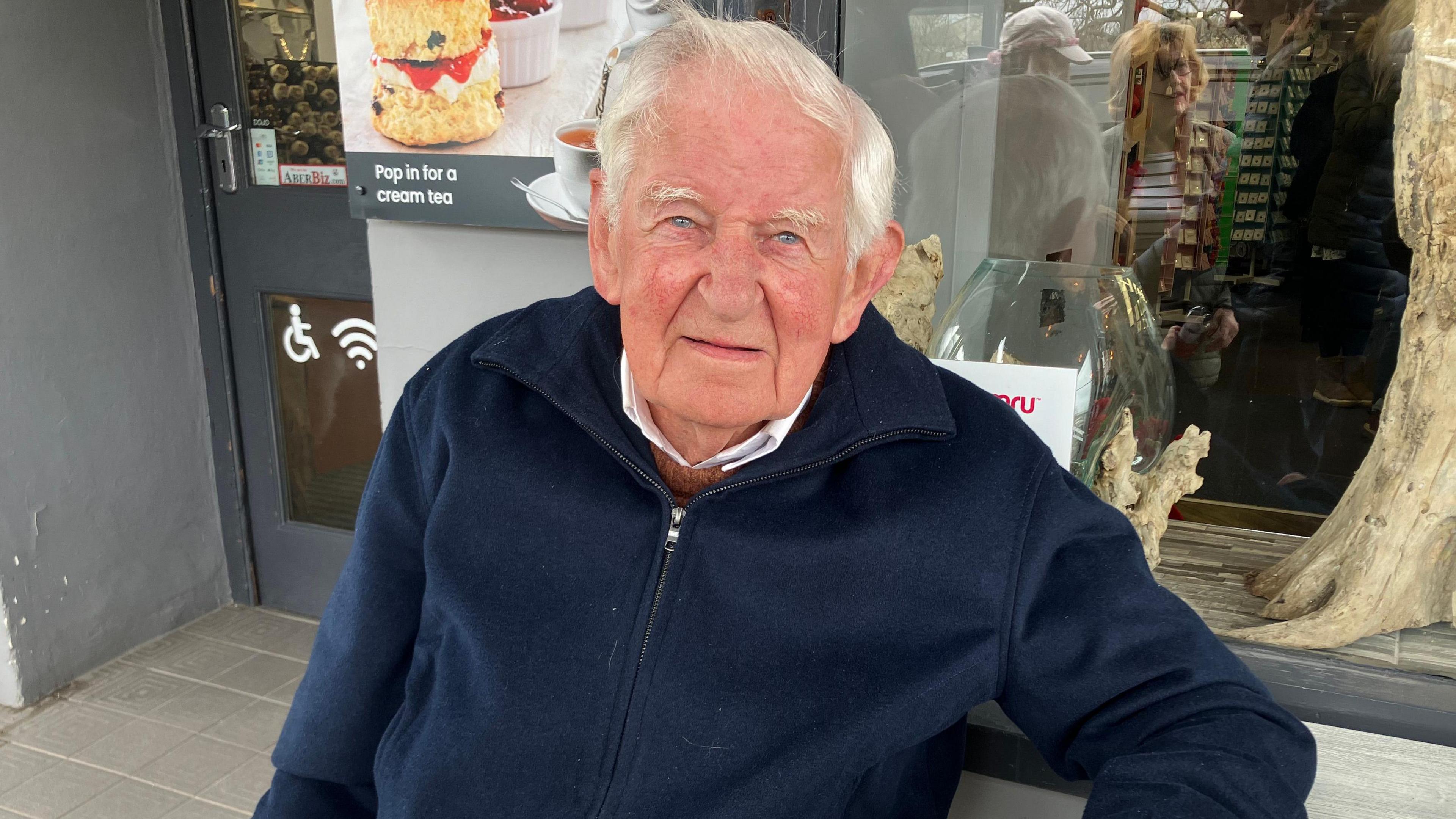 Alfor Jones yn eistedd gyda phaned yn Aberaeron