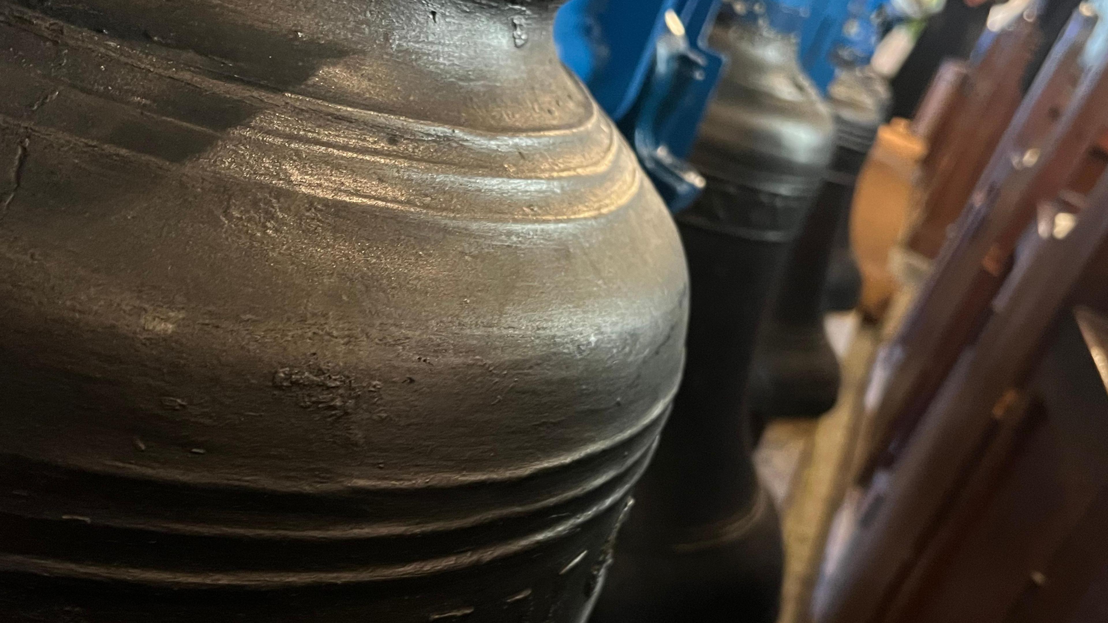 Close up of a large bell with lines around the instrument. Blurred church pews can be seen next to the bell.