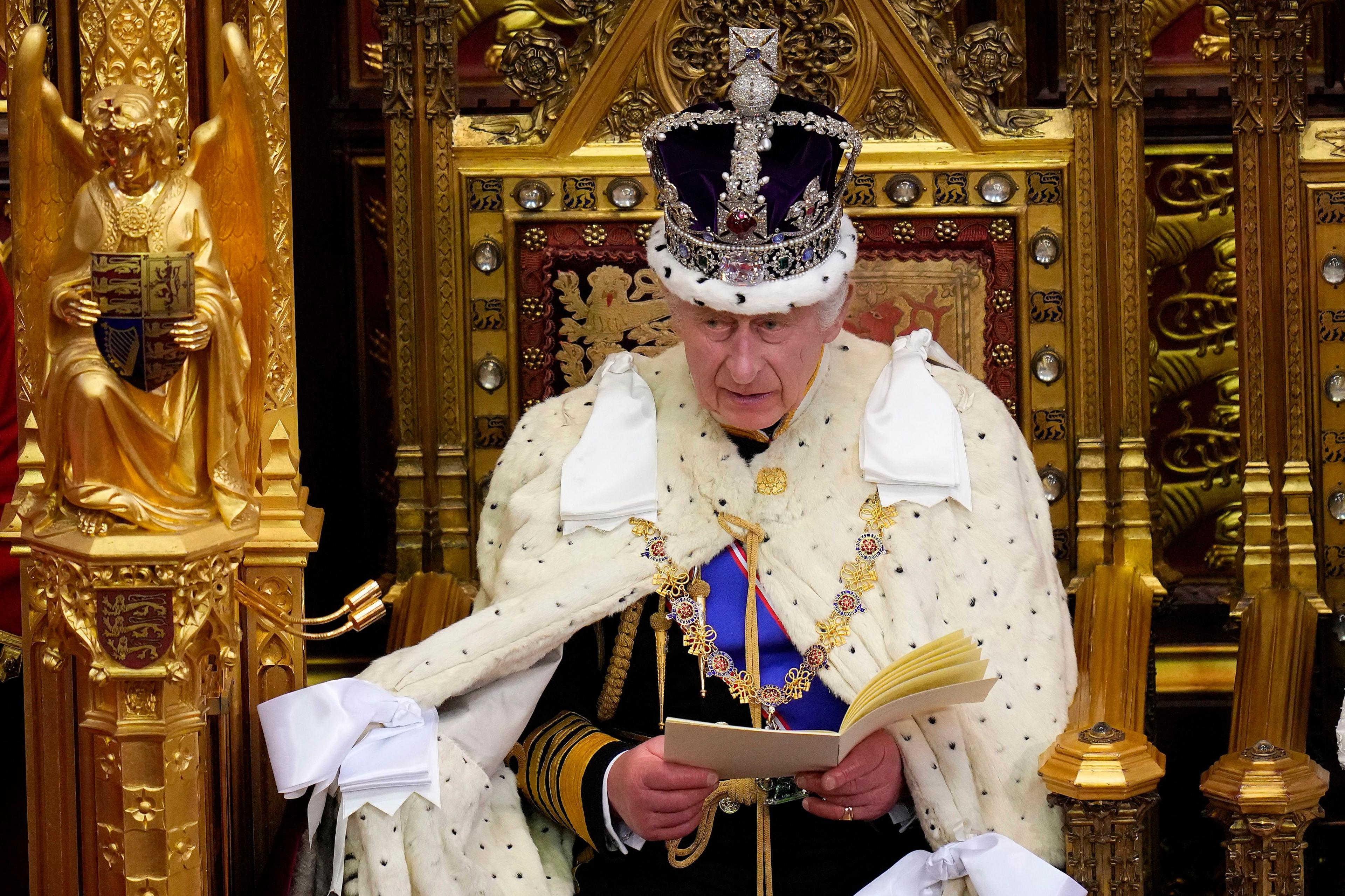 King Charles sits on a golden throne wearing the crown jewels, reading a speech