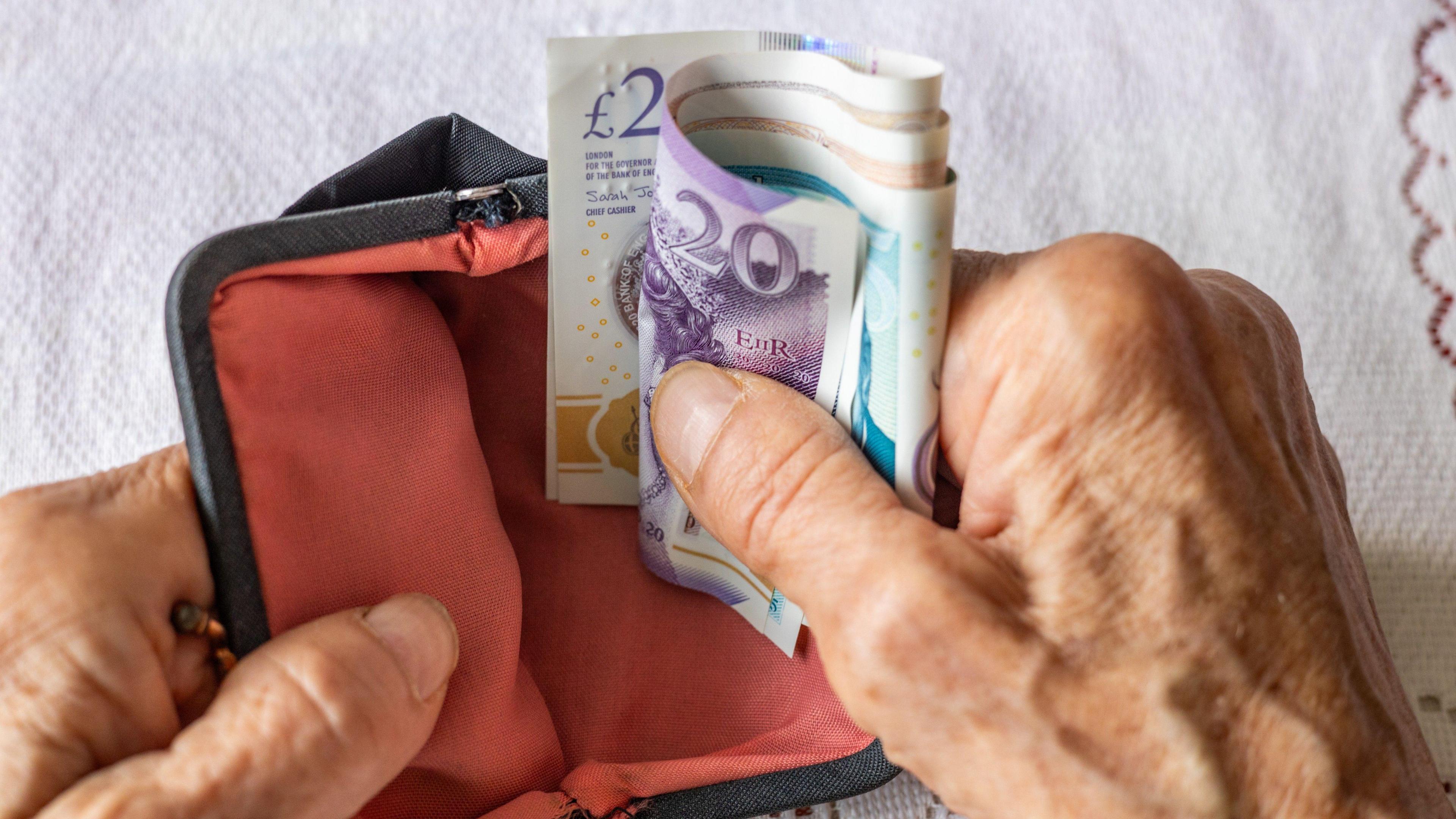 A pensioner's hands counting bank notes over an old-fashioned purse.