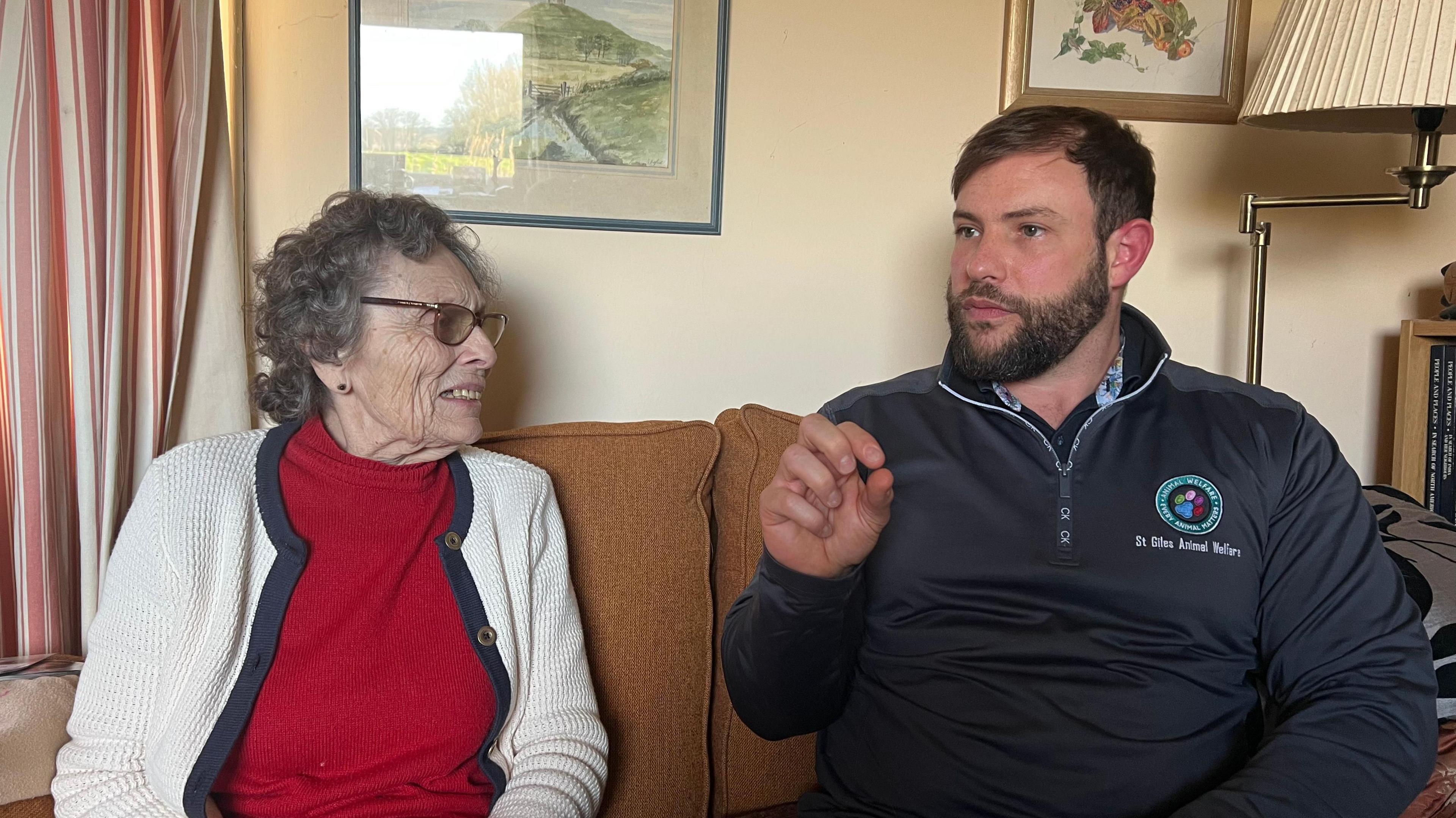 A women in a red jumper and cardigan sitting next to a man in a jumper saying St Giles Animal and Rescue Centre.