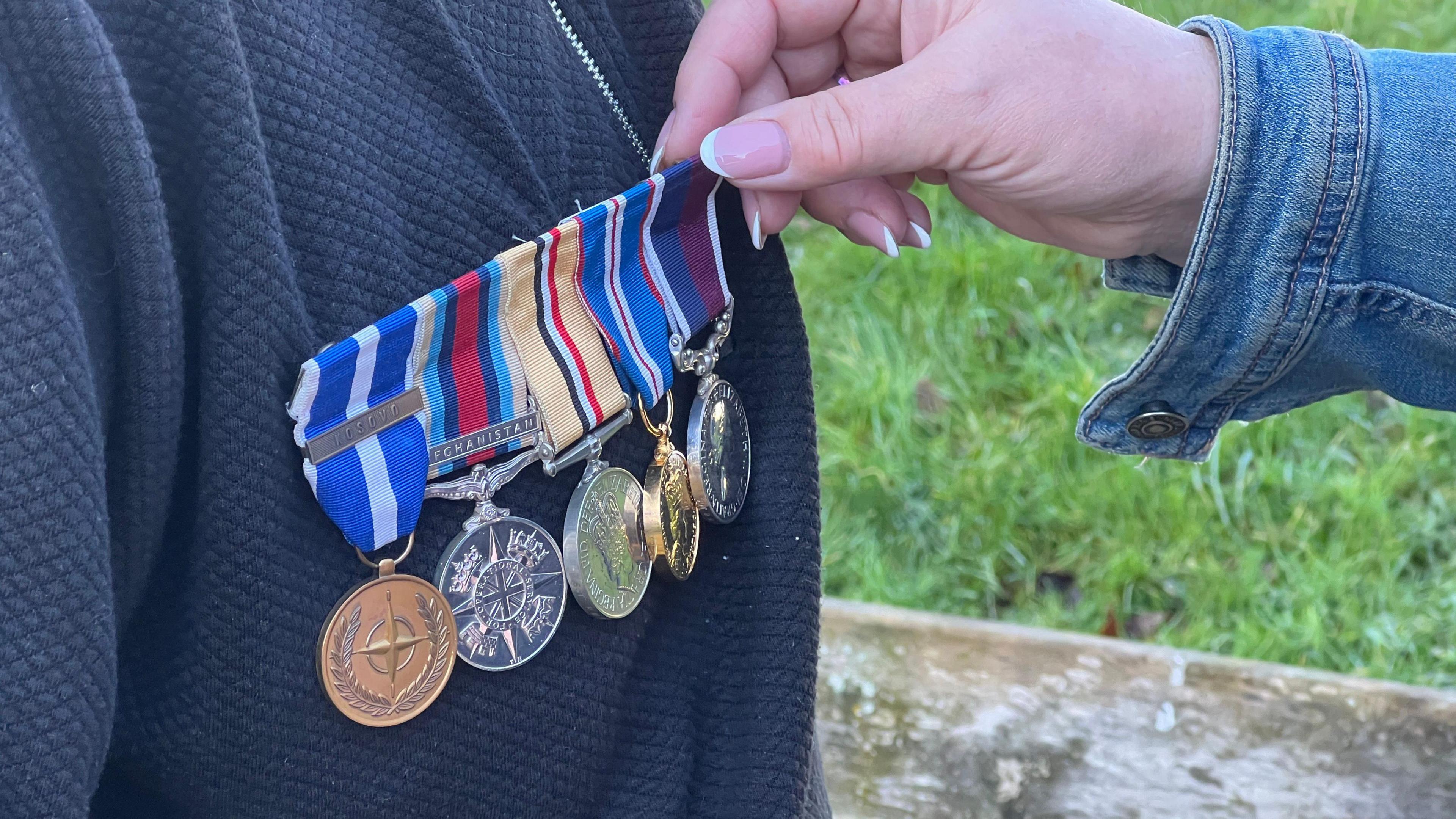 Five service medals on a jacket. They are a mixture of bronze, silver and gold. A woman is touching them.