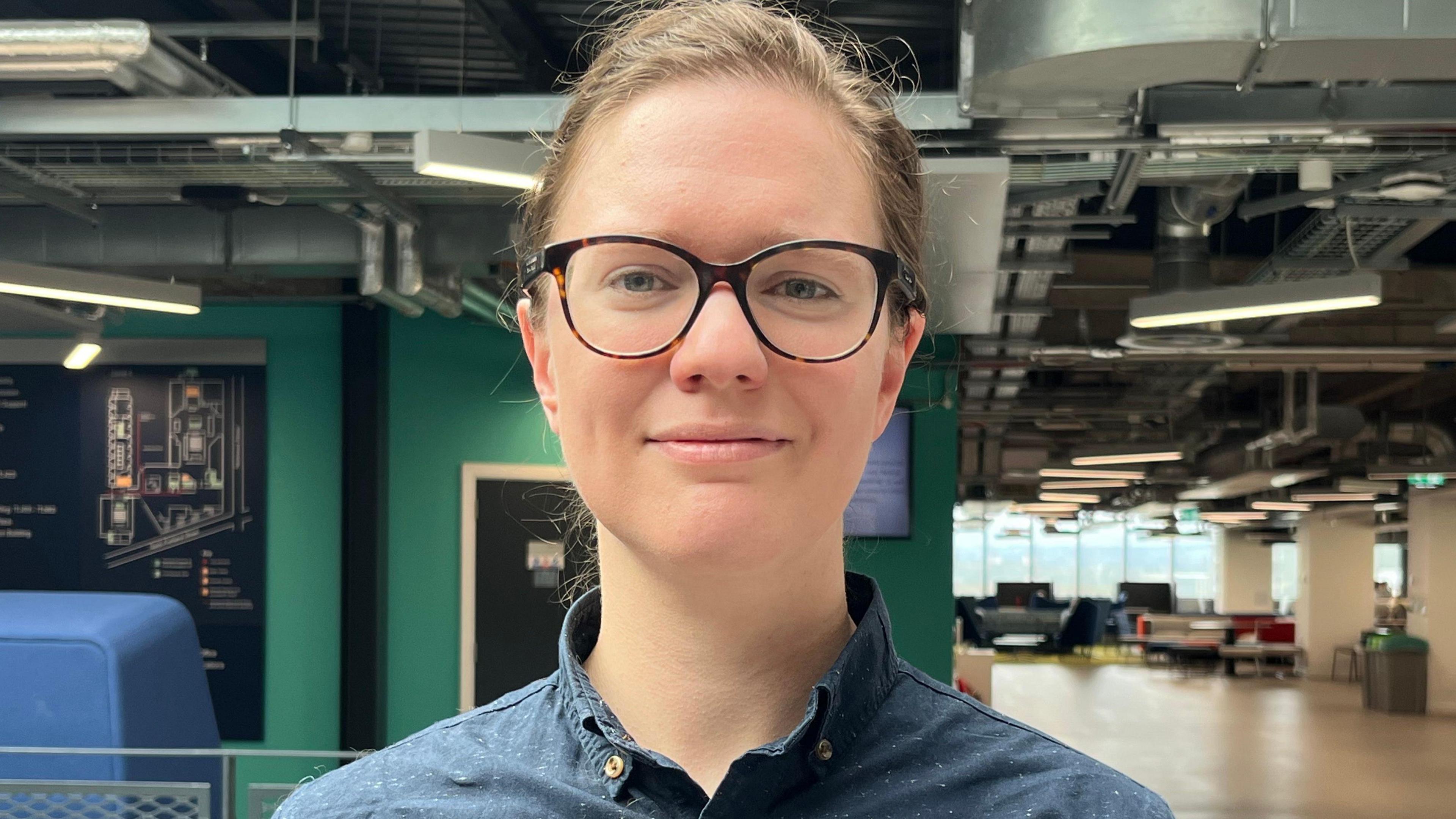 Hannah Rudolph, a young woman with brown hair and glasses, pictured in a modern office building