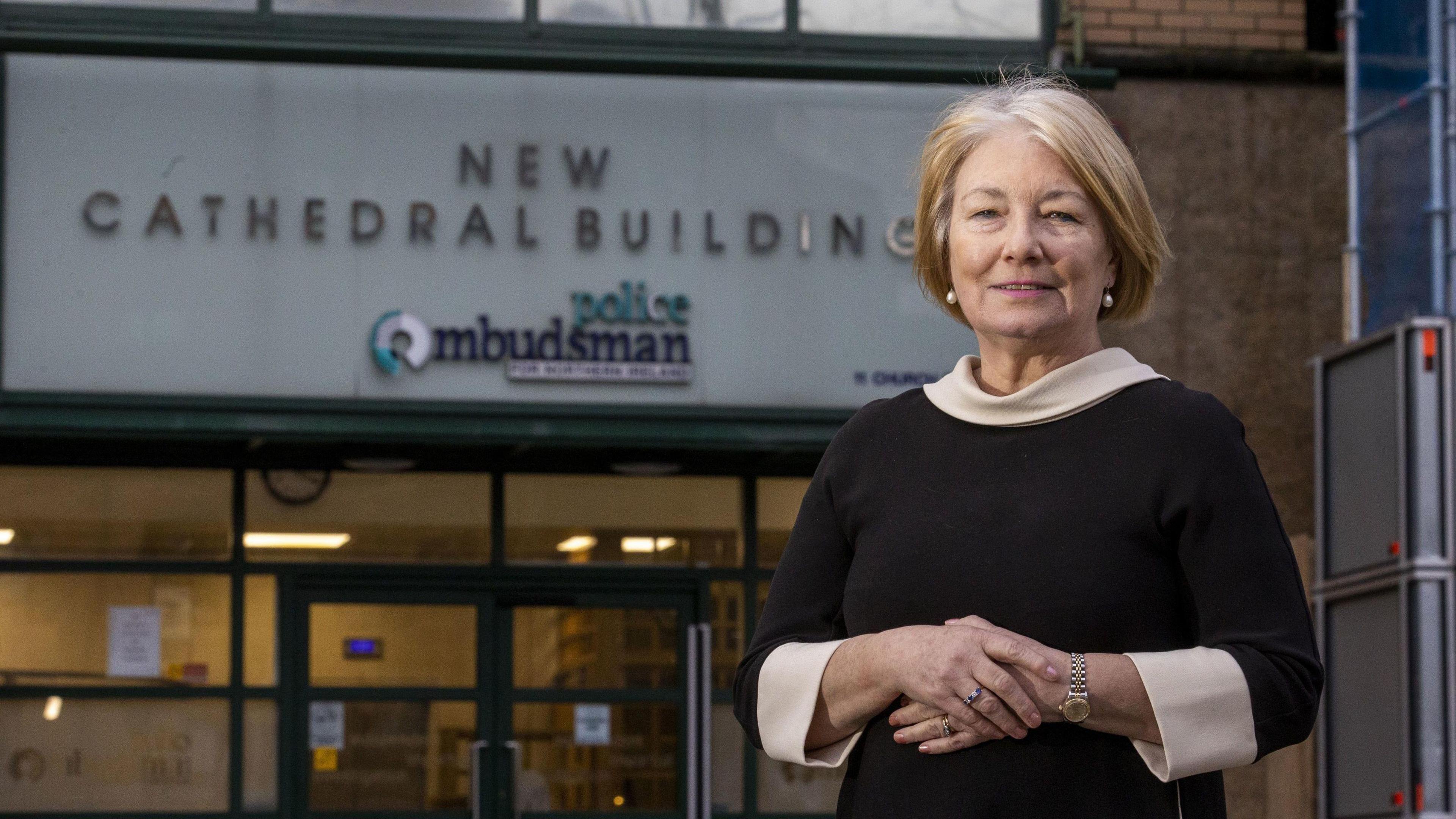 Police Ombudsman Marie Anderson standing outside the office of the Police Ombudsman in Belfast.  She has short, blonde hair and is wearing a black dress with a pale collar and cuffes. 