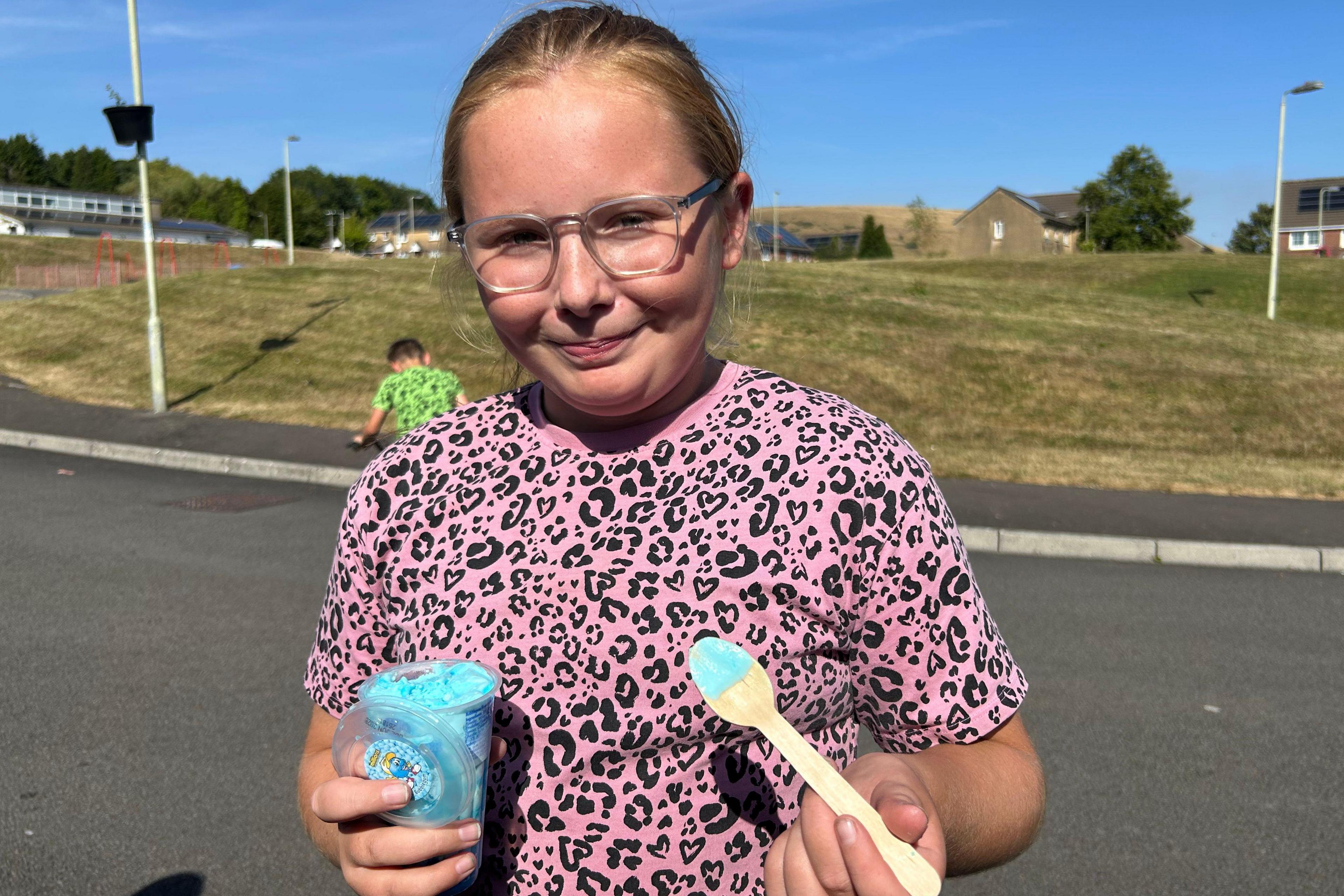 Eleven year old Lexi. She is wearing a pink t shirt and glasses, holding a blue ice cream.
