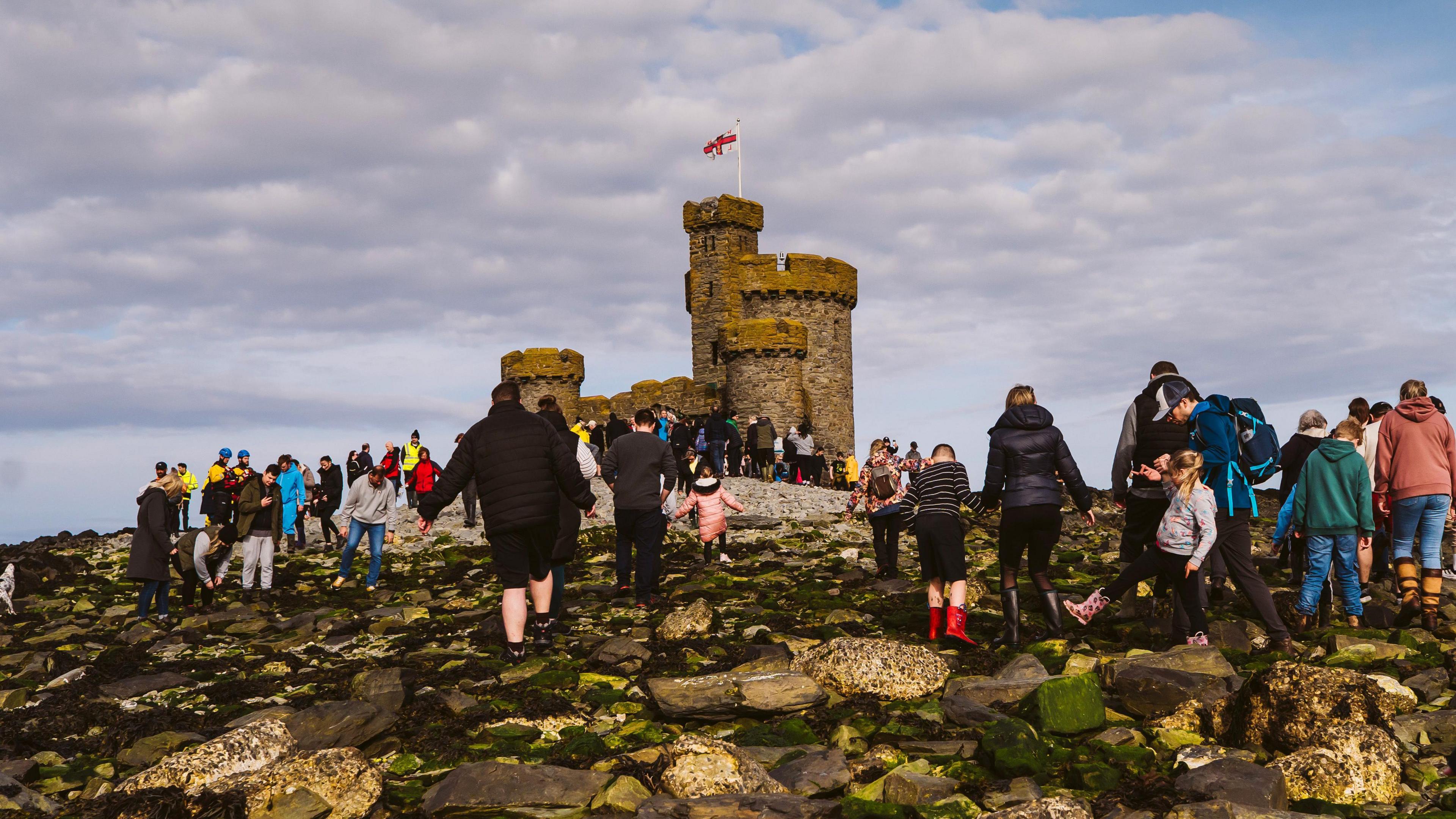 A large crowd of people walk up the rocky terrain to the Tower of Refuge.