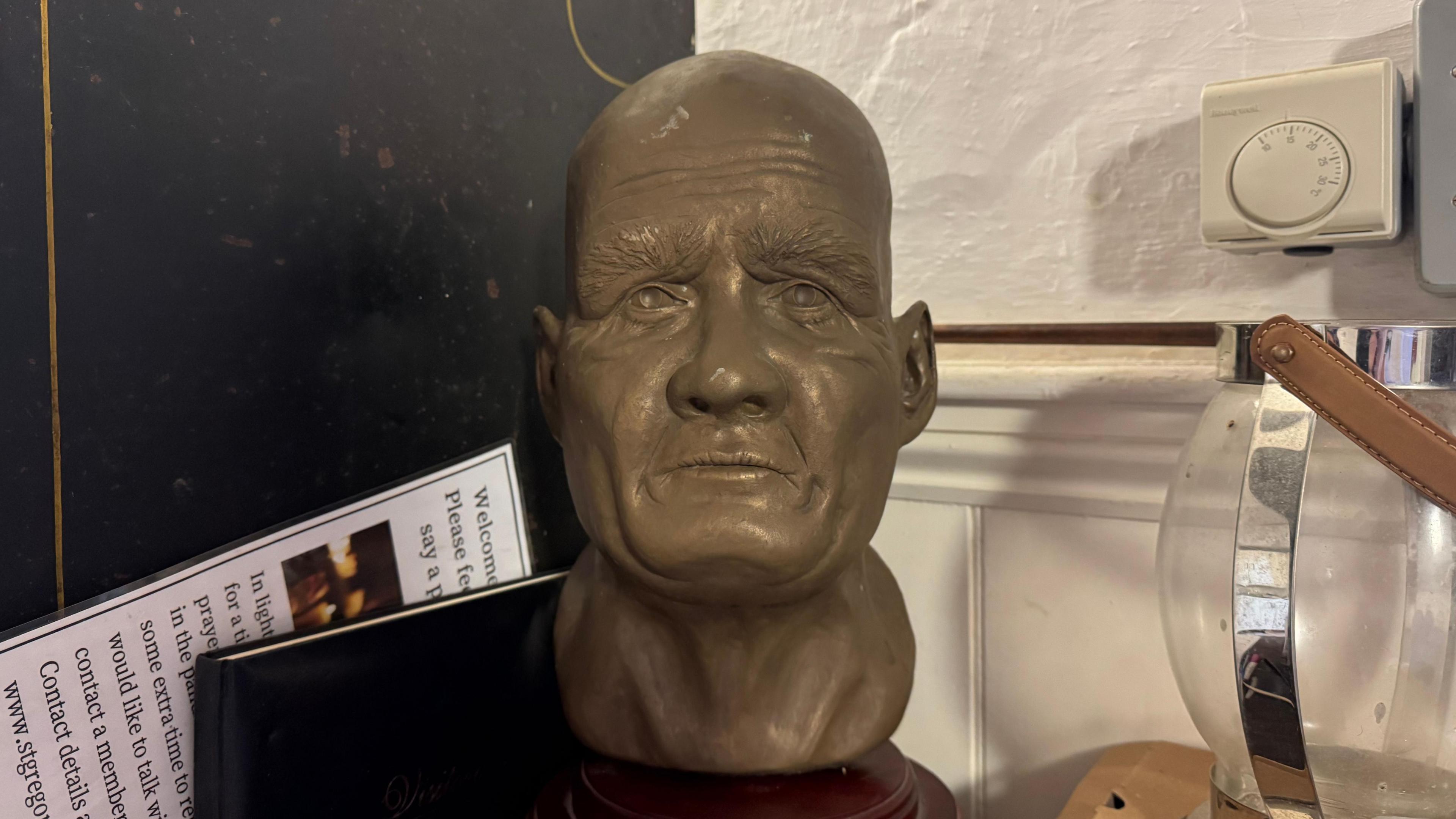 A bronze bust of Simon of Sudbury's head. It sits on a dark wooden block.