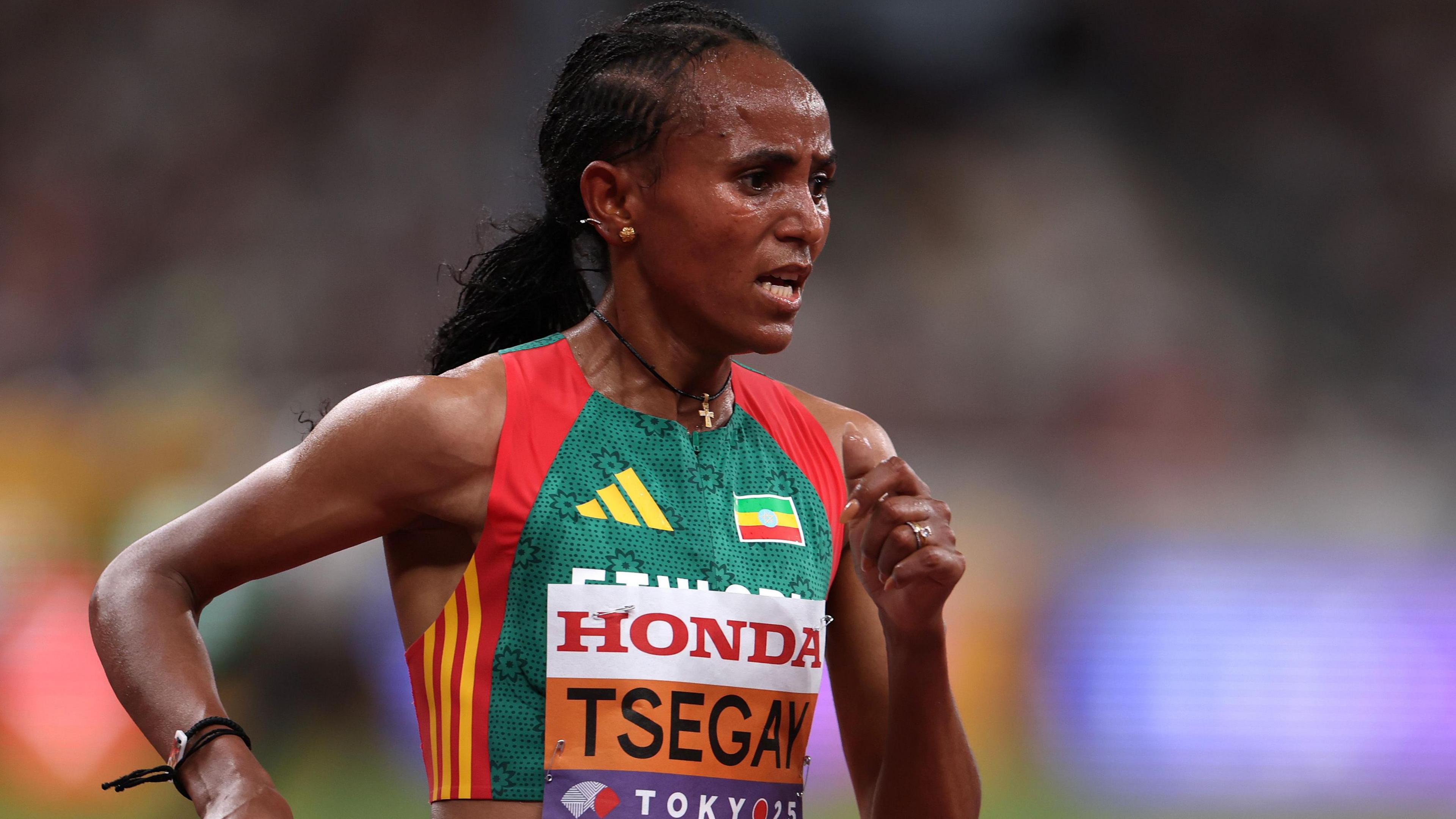 Gudaf Tsegay is seen from the waist up wearing an Ethiopia running vest with a bib with her surname and the Tokyo 2025 logo on the front of it. She looks foward in concentration while she runs