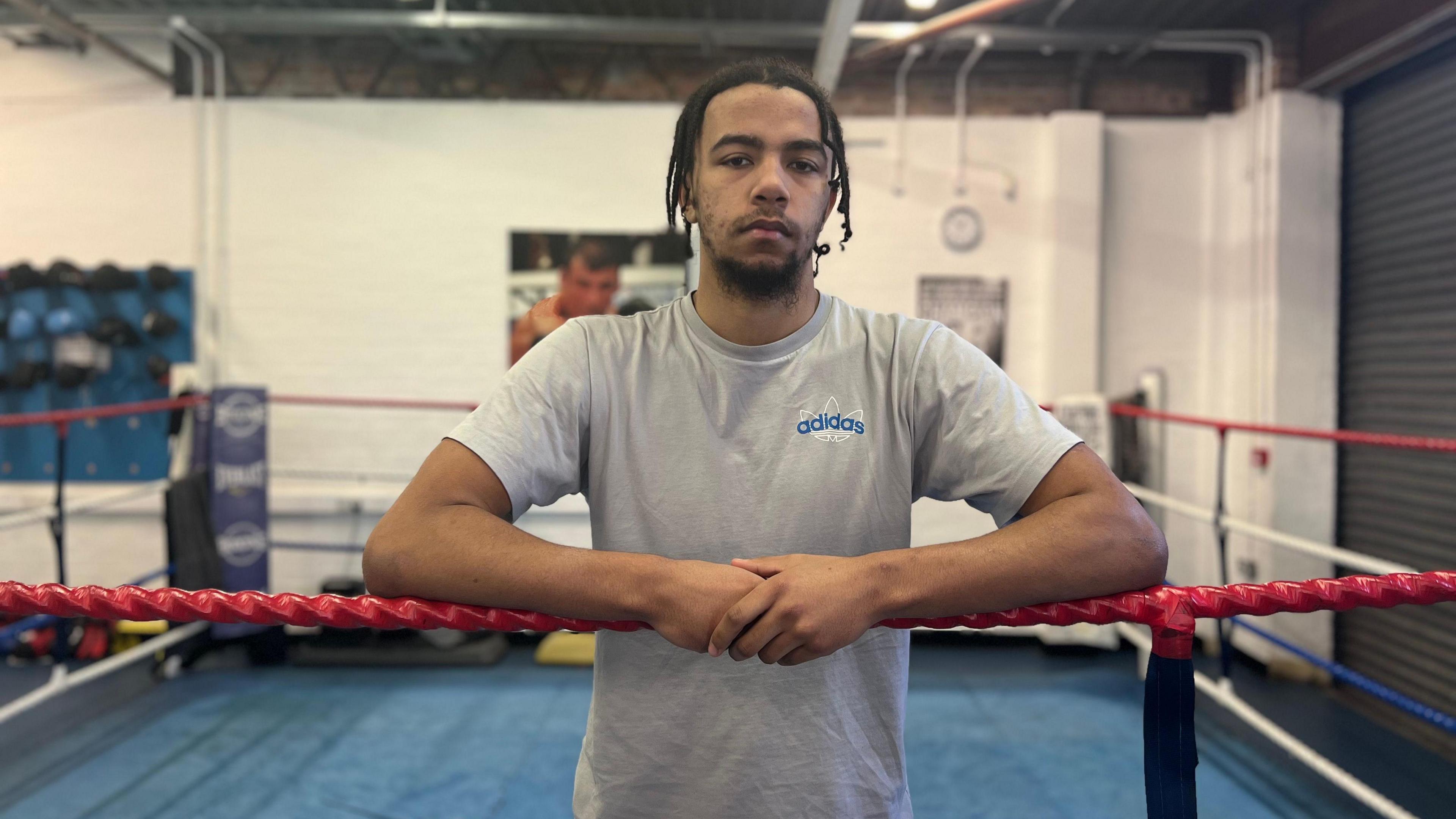 Marcel is standing in a boxing ring. He's arms are draped over the ropes 