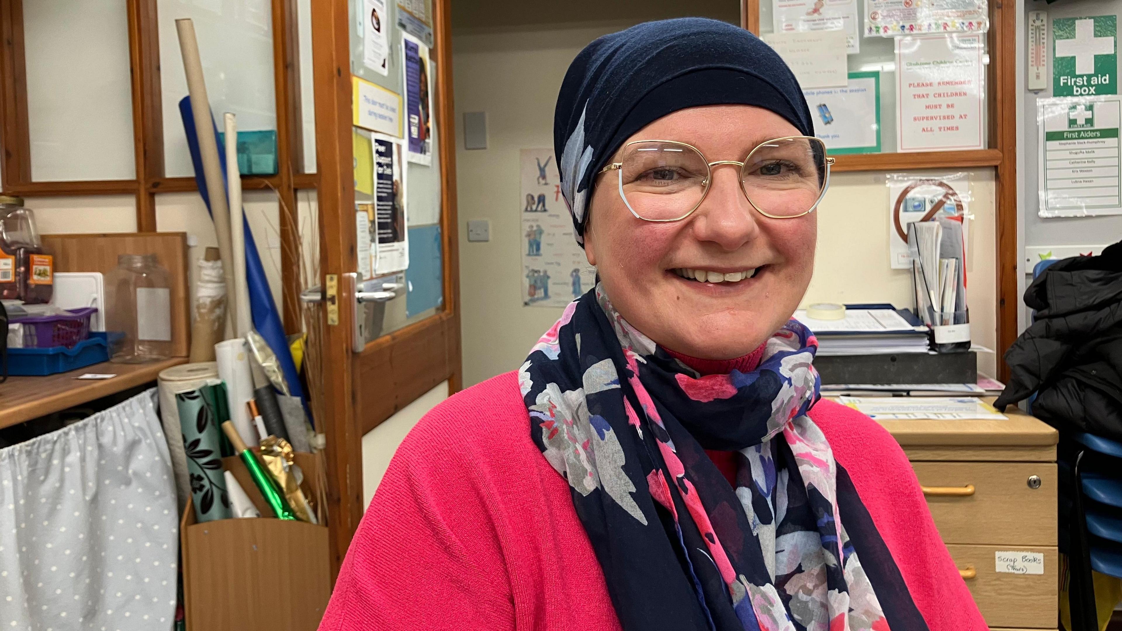 Natalia wearing a pink cardigan with a navy blue headscarf and a blue and grey floral scarf 