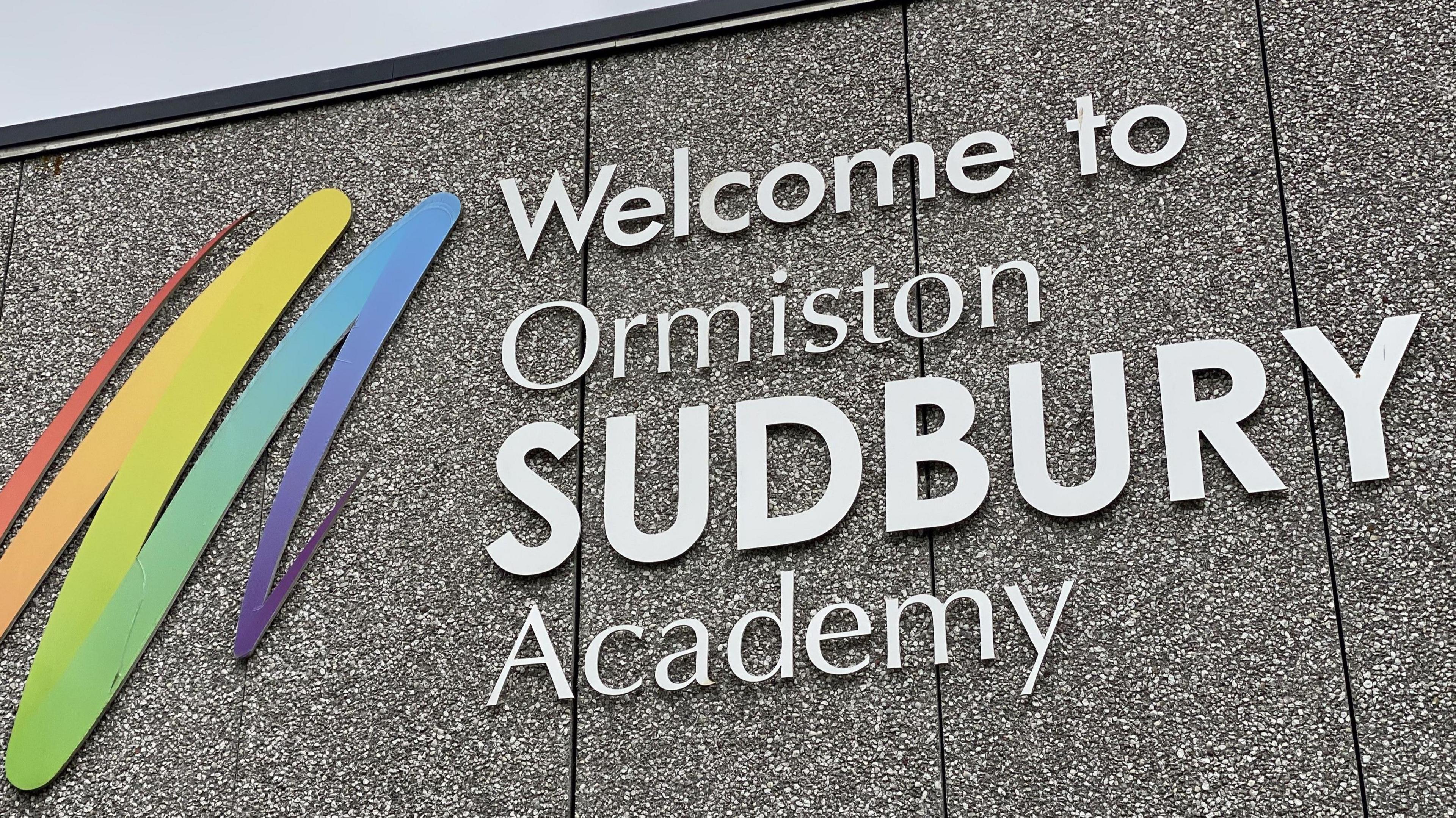 A closer view of the school's welcome sign fixed to the side of its grey building.