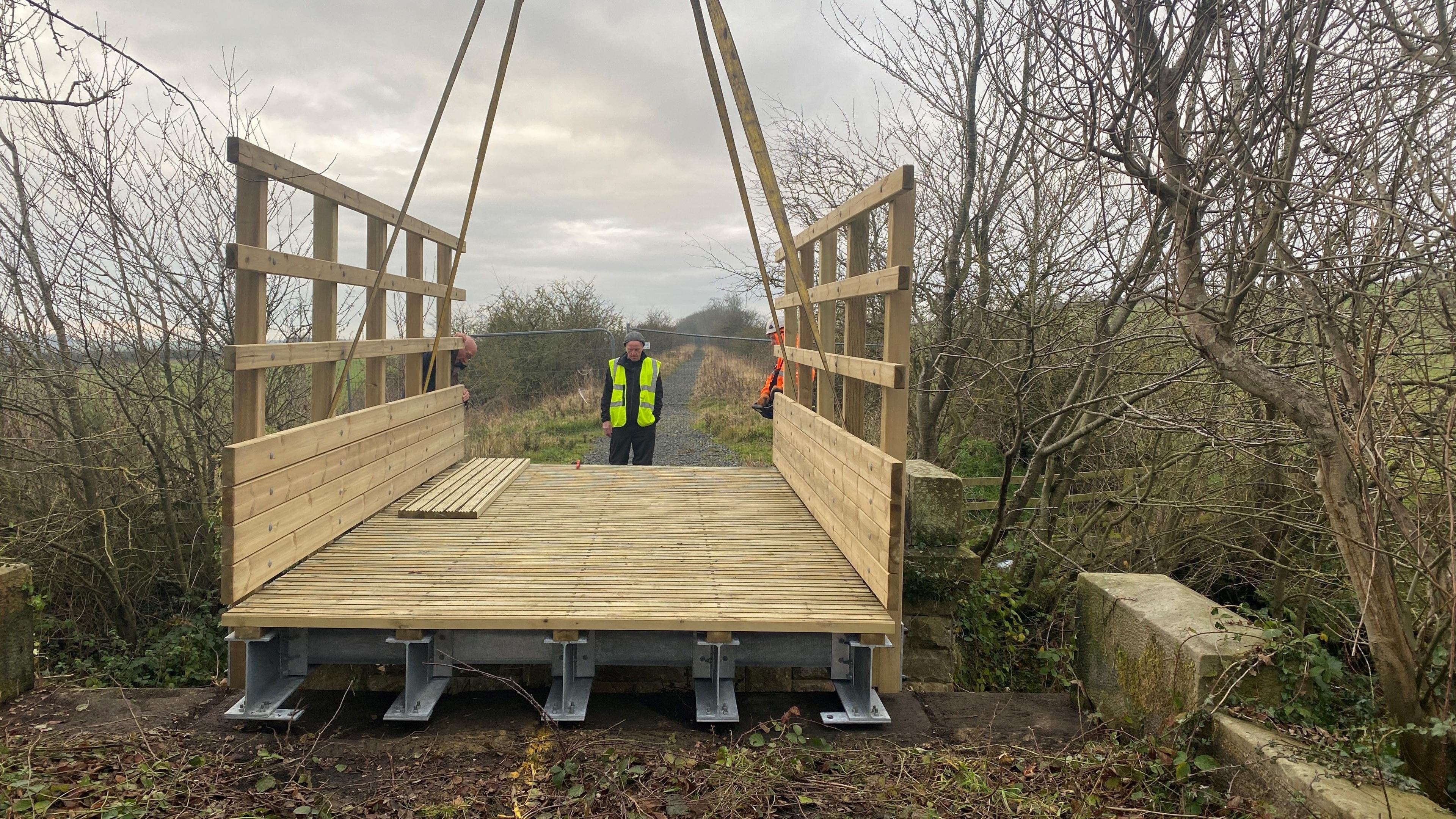 A new bridge made of wood with a metal base sits on a narrow gap between two sections of a former railway 