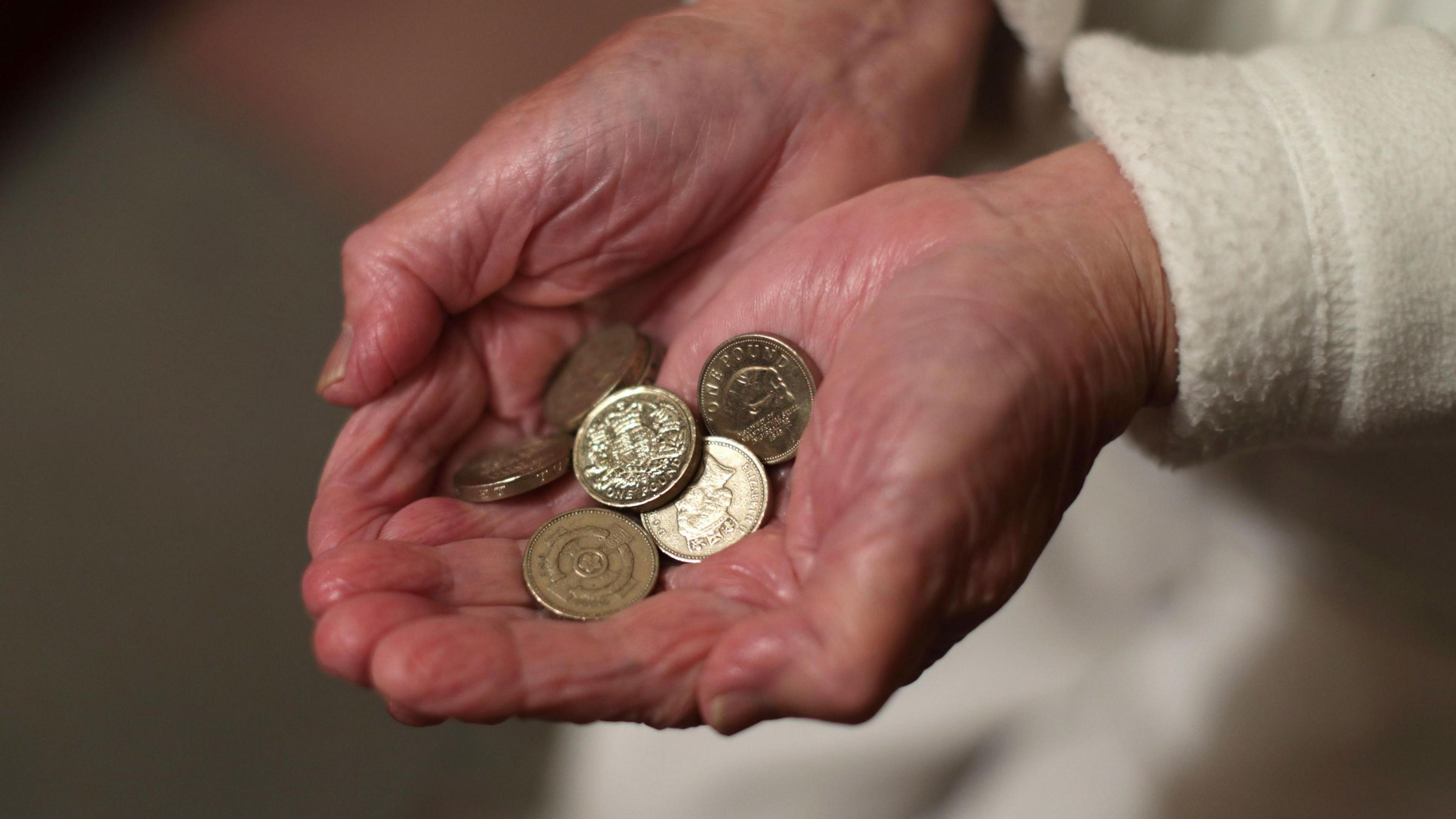 An elderly woman holding pound coins in her hands - just her hands are visible