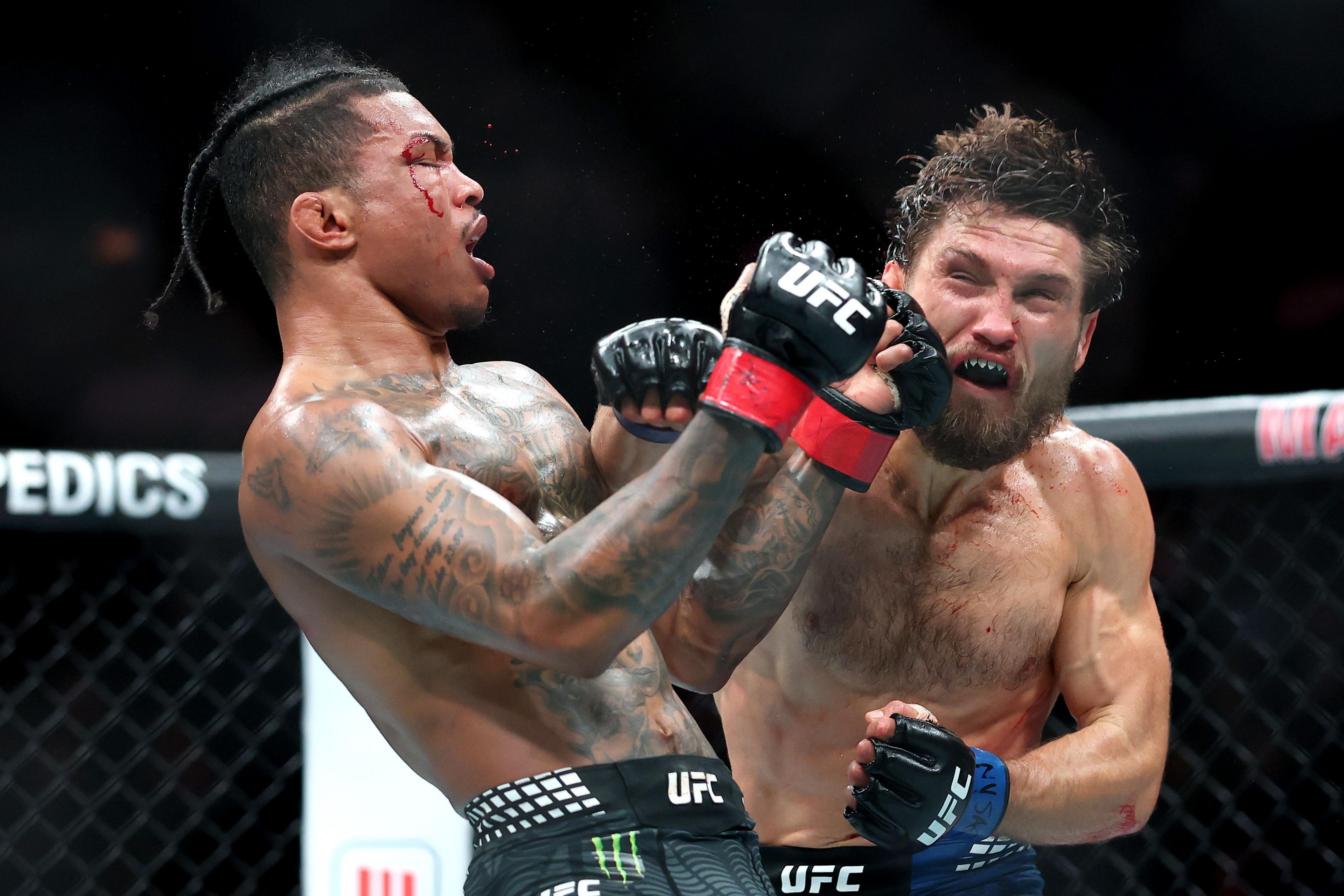 Two UFC fighters in an octagon, one delivering a punch to the other’s face, both wearing gloves and shorts with visible branding, under bright arena lighting.