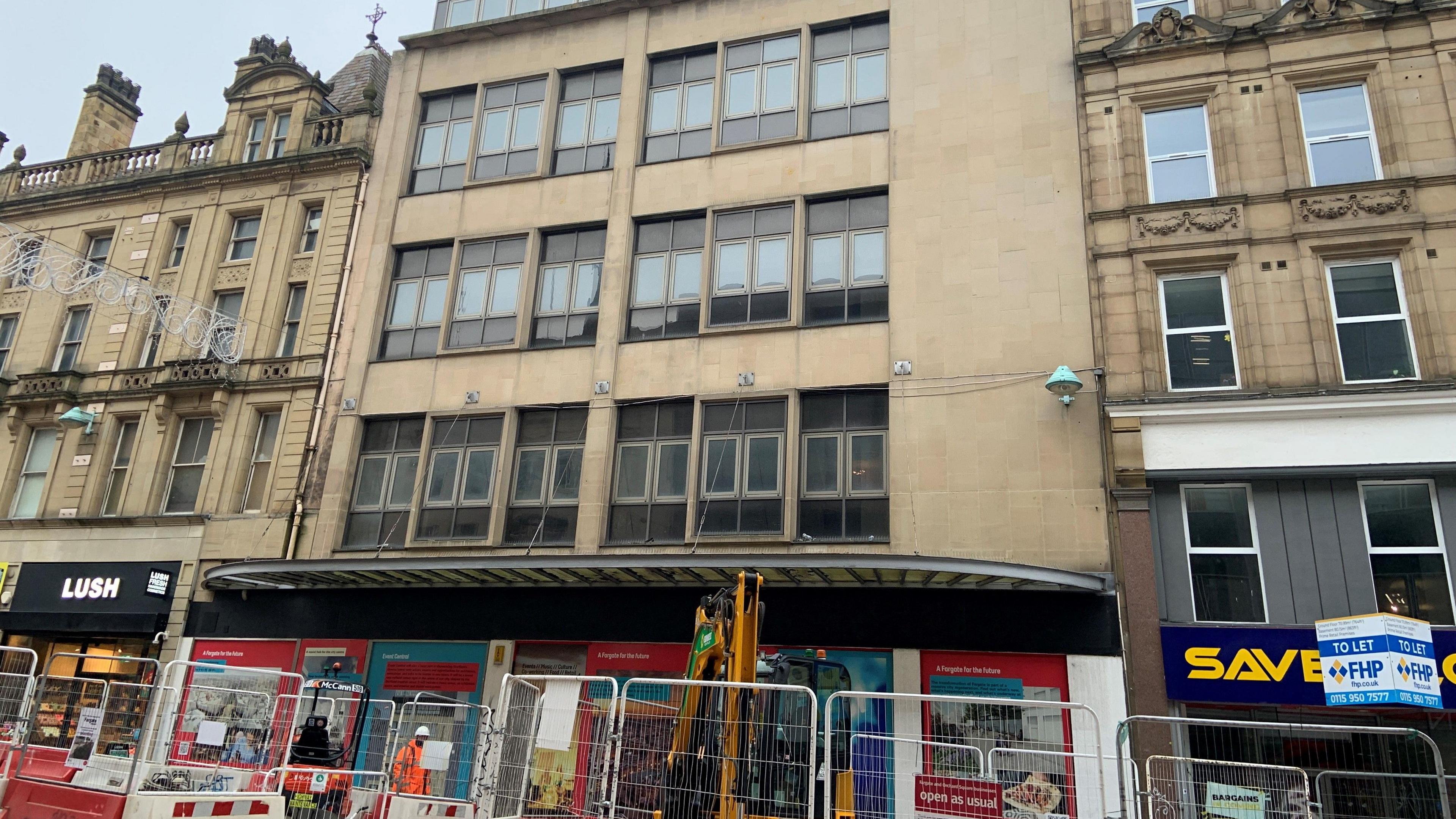An empty building on Fargate in Sheffield city centre, which is made a stone with several large windows. There are building works on the pavement outside