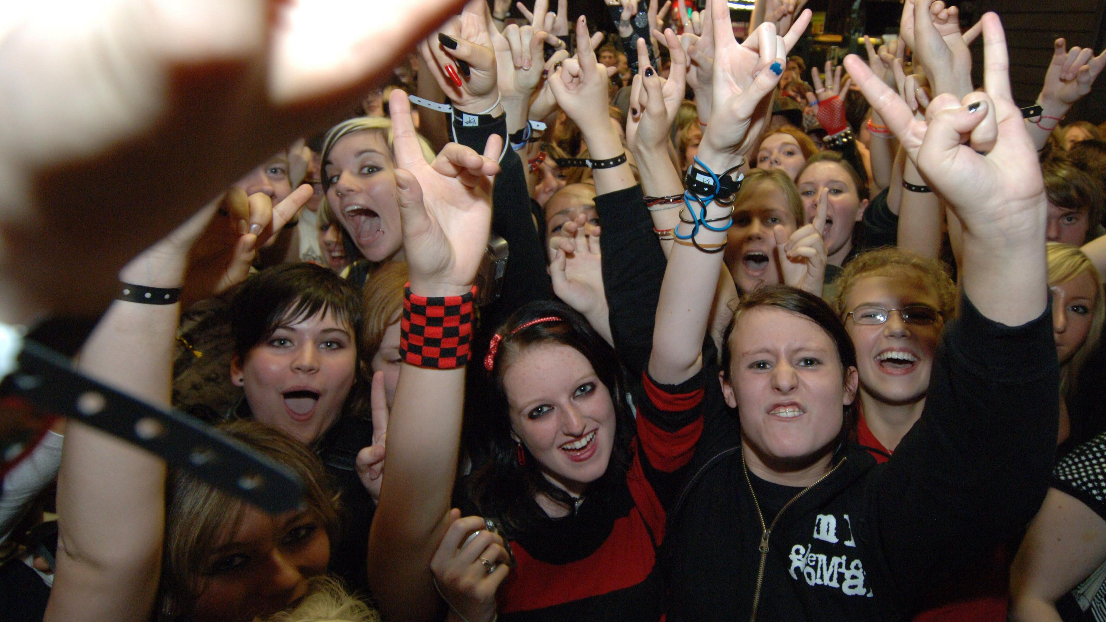 An image of youth at a concert with their hands displaying a rock sign.