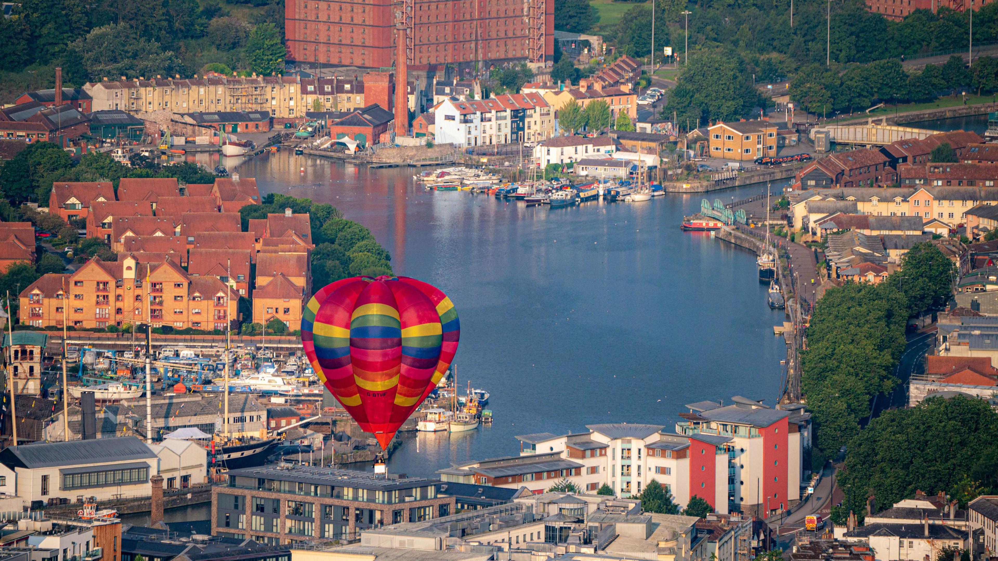 Red balloon flying over Bristol harbourside with businesses and homes in the background.