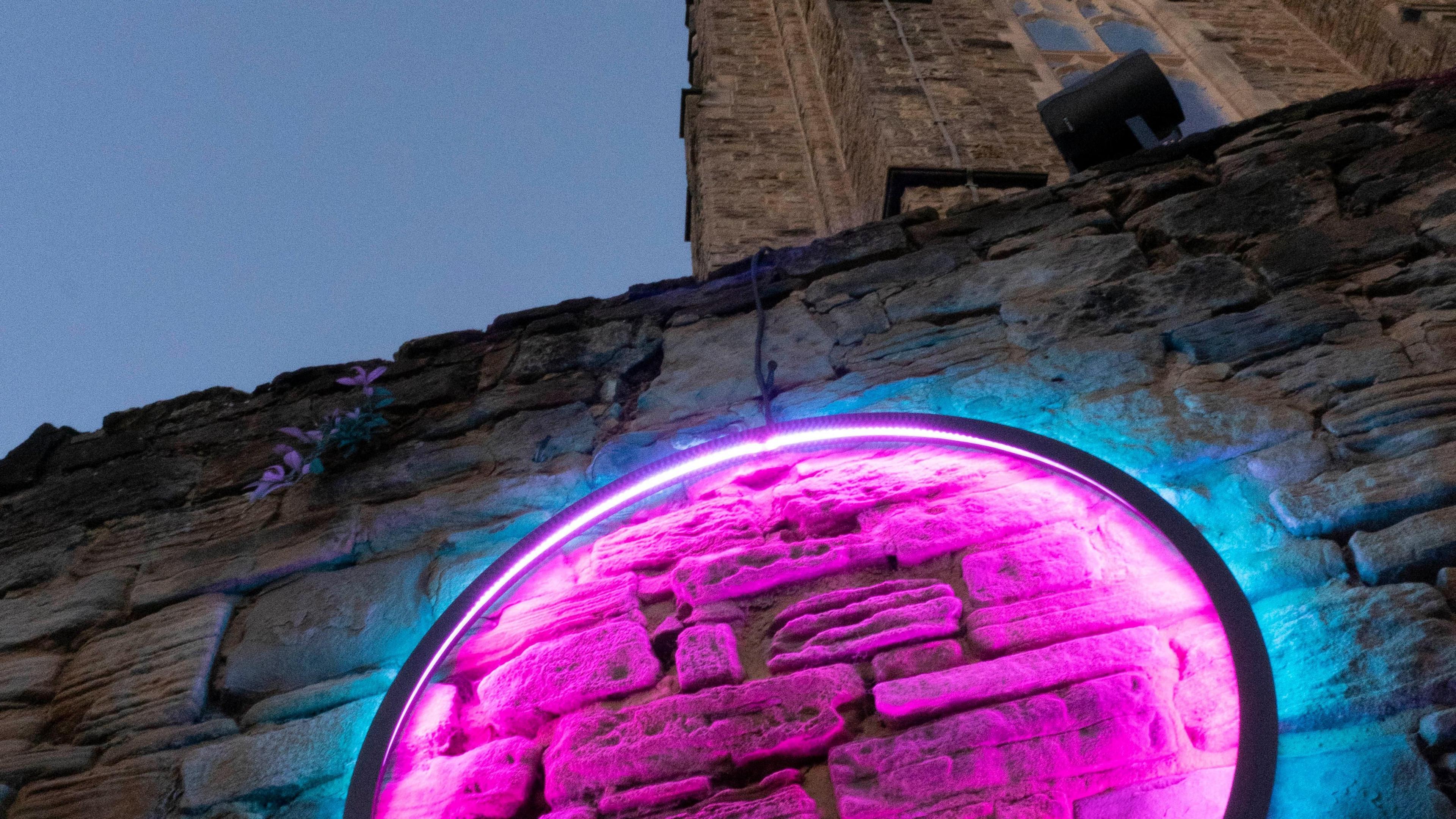Part of a circle is illuminated on a wall. Its inner is pink in colour, with the outside blue.