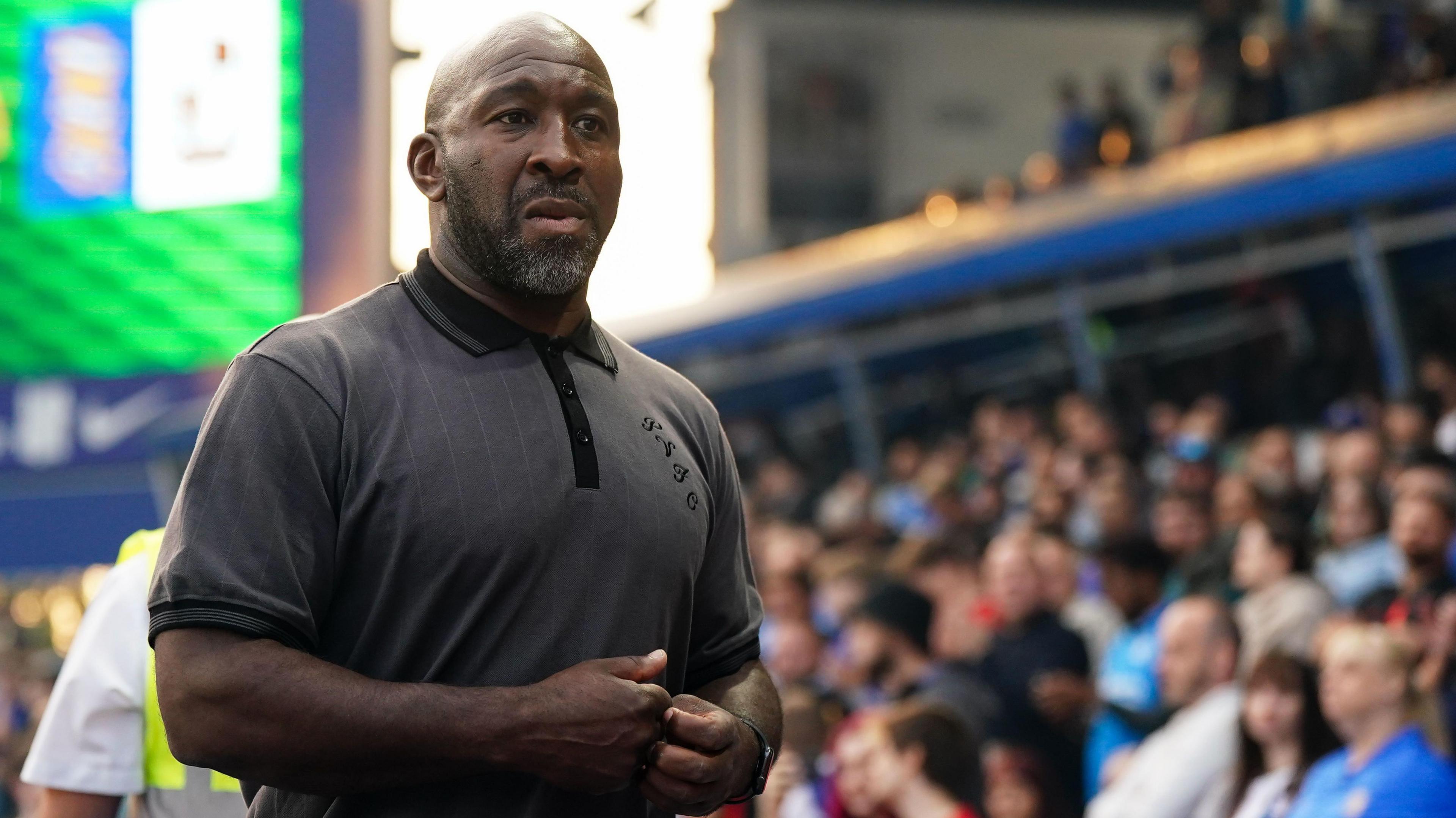 Darren Moore walks towards the dressing room along the touchline during a match. He is wearing a grey T-shirt
