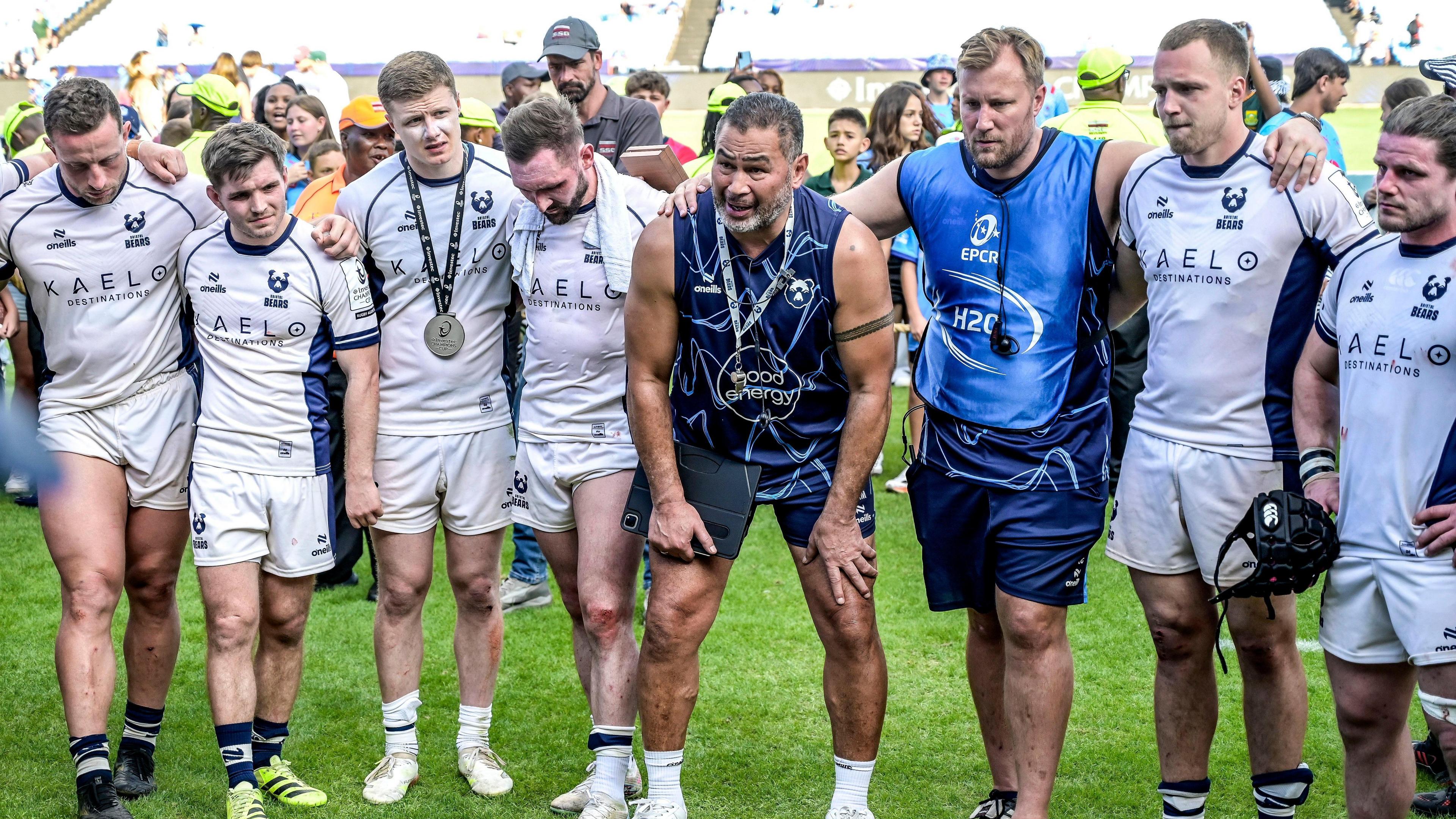 Pat Lam (fourth from left) stands with his hands on his knees surrounded by four players to his right, and a coach and two more players to his left, as he leads a post-match huddle on the field following their win against Bulls in Pretoria