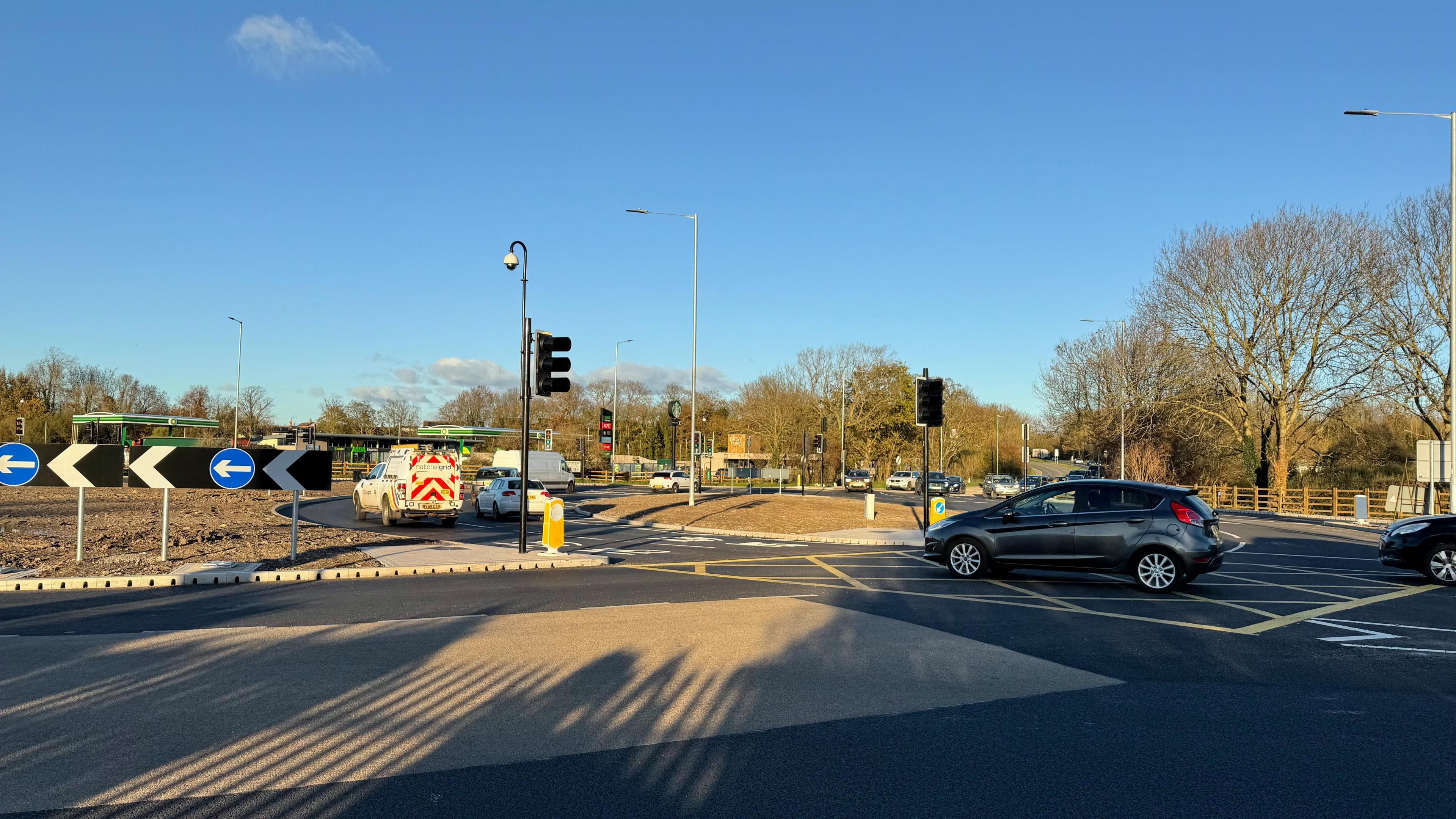 The Dunball roundabout with cars going around it. The sun is shining on the tarmac.