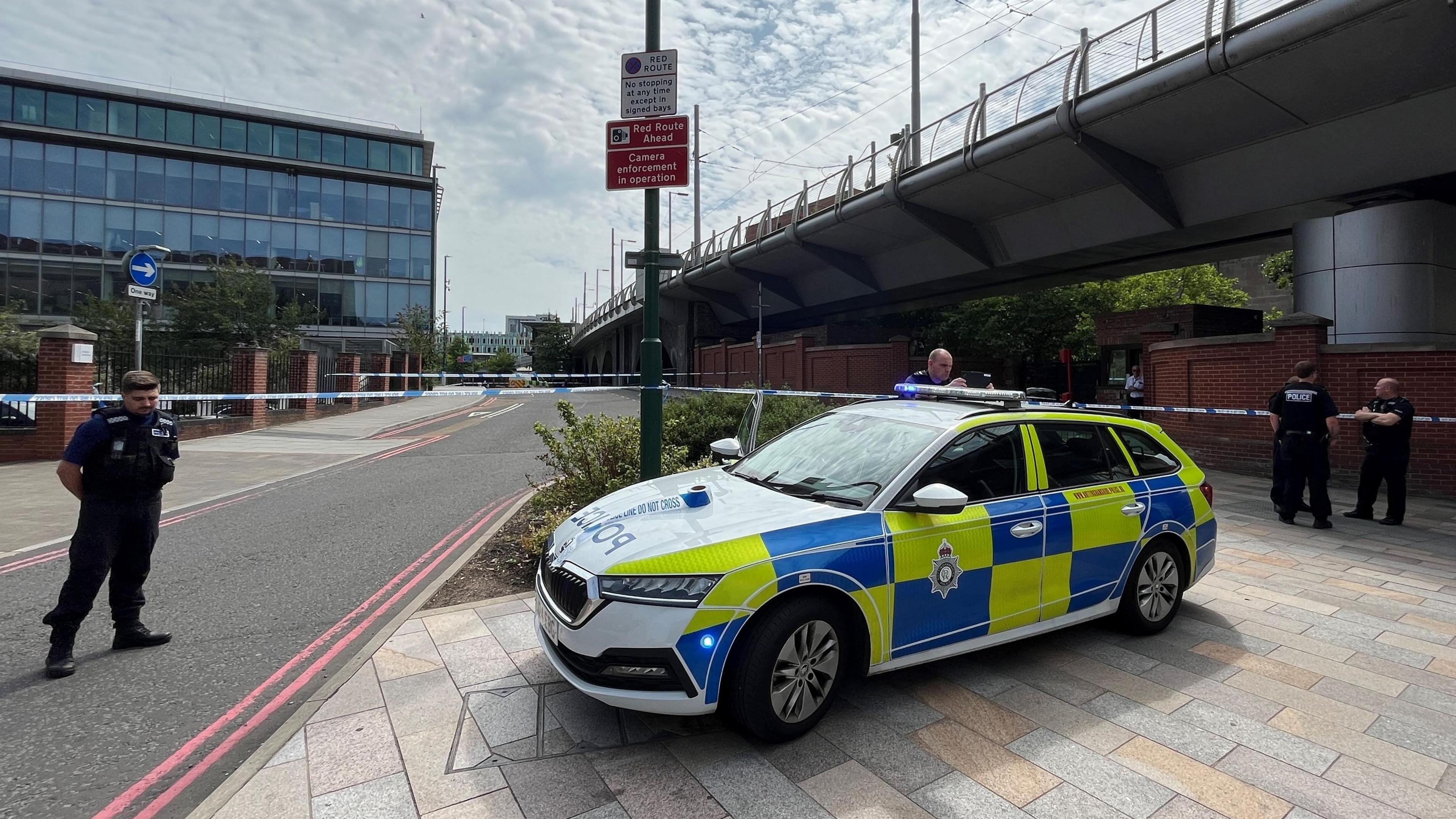 A police car in front of a cordon with officers in attendance