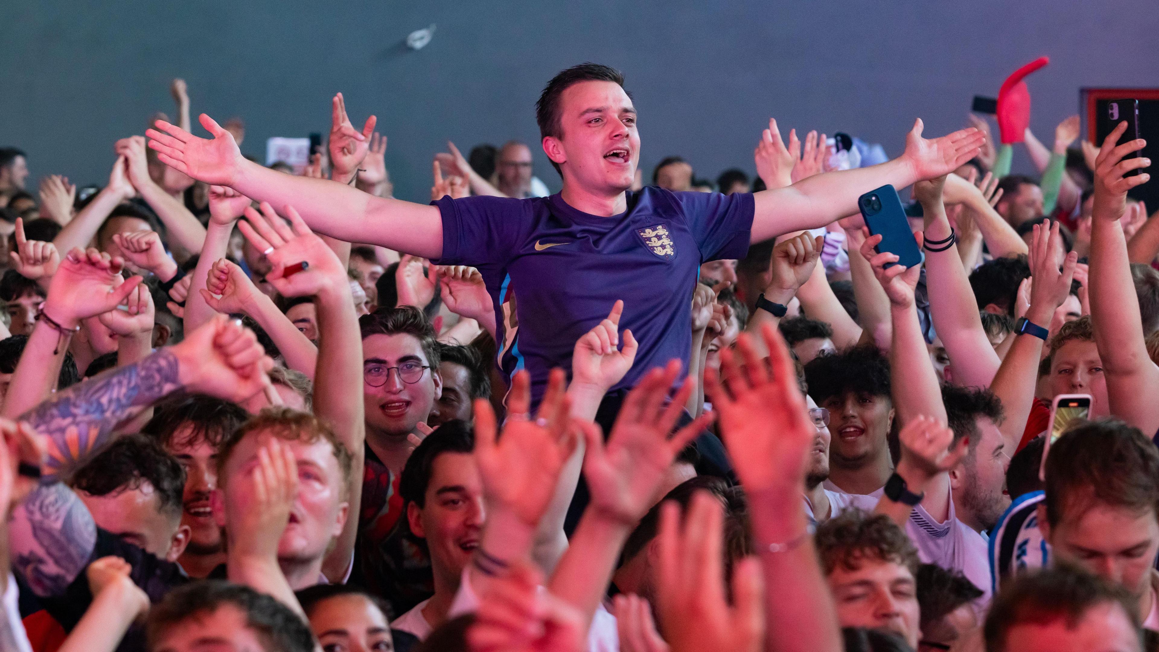 A crowd of England fans celebrate with their arms in the air