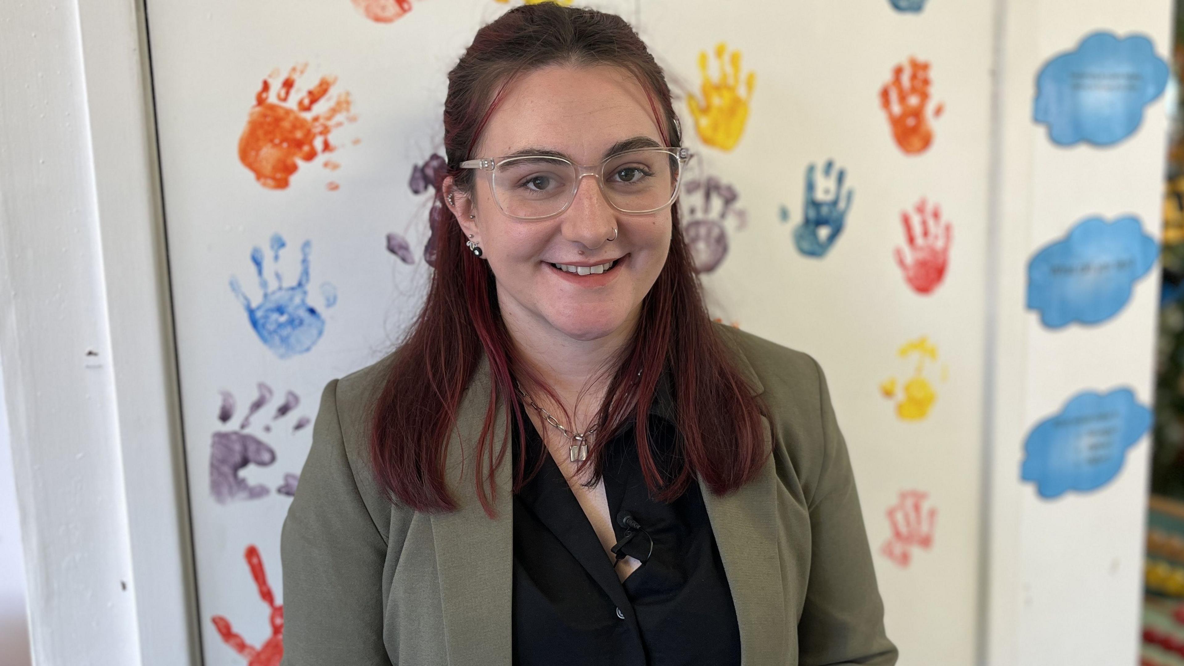 Manager of Rainbow Early Years, Hayley Galliers, smiling in front of a wall covered in children's hand prints