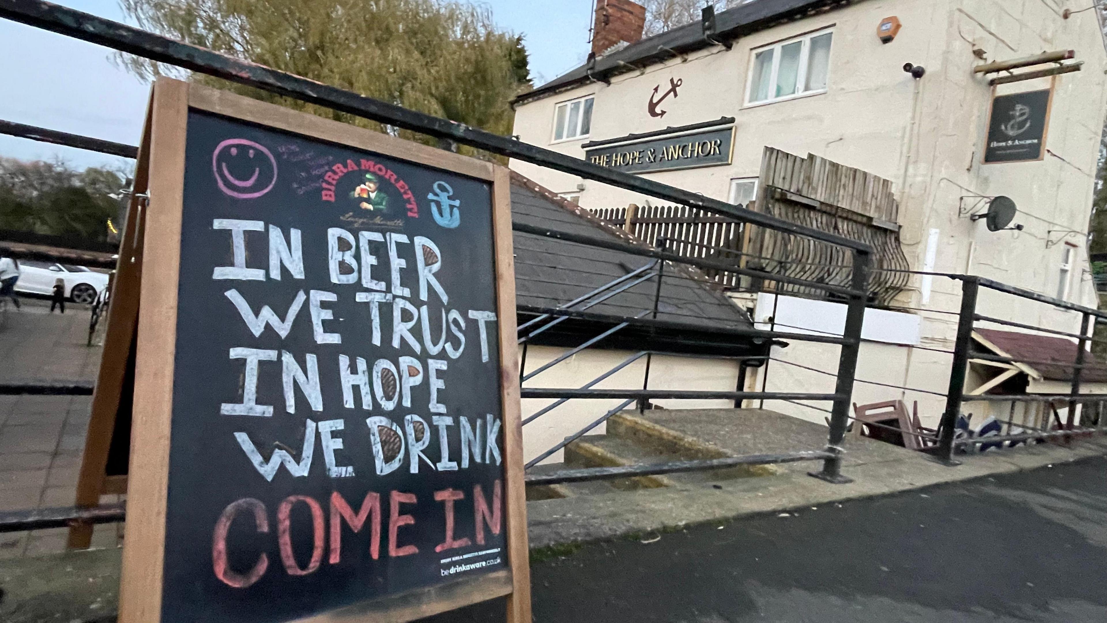 A pub blackboard outside the venue saying 'In beer we trust in hope we drink. Come in."