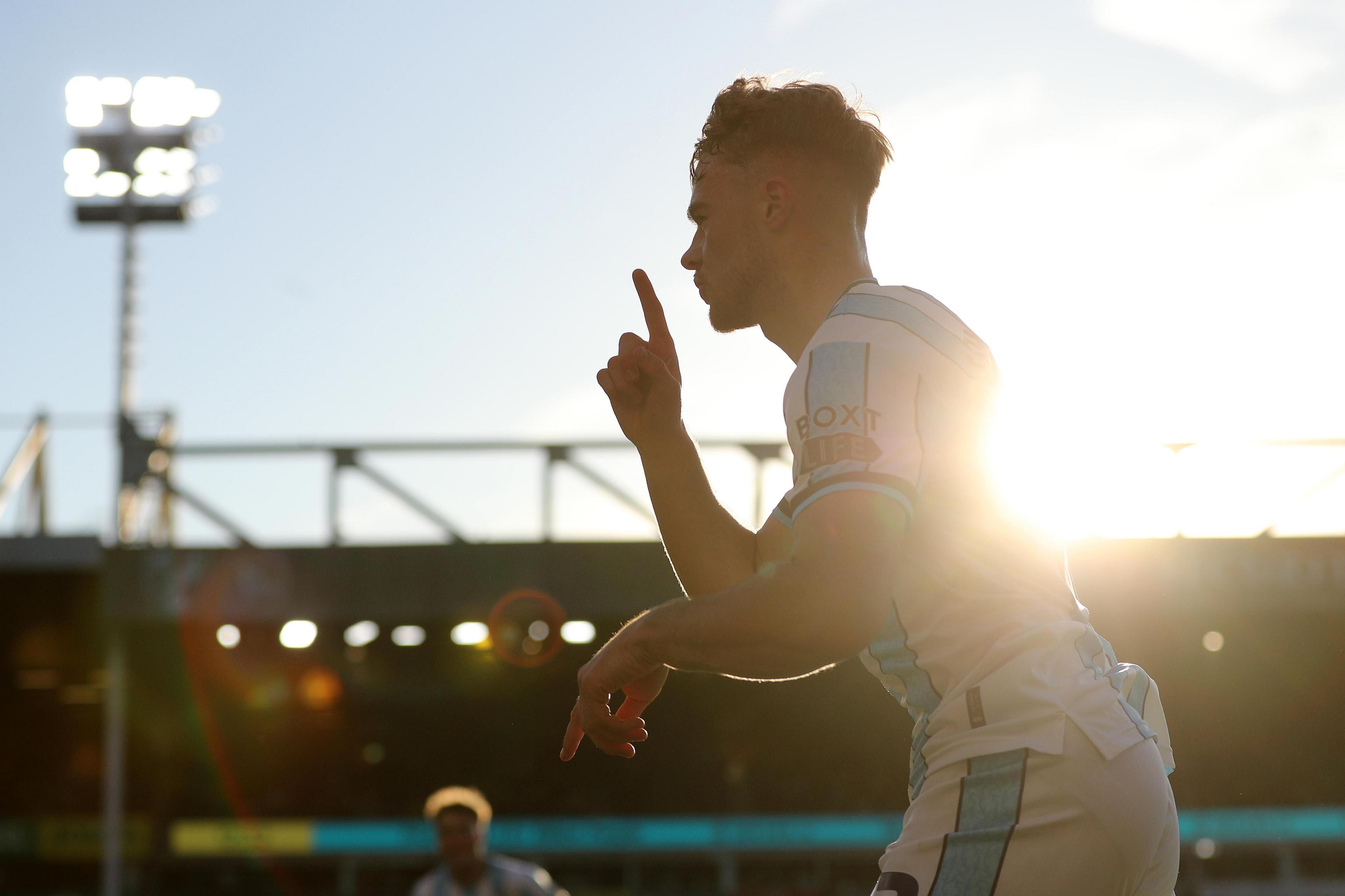 A footballer in a blue and white striped Middlesbrough away shirt shirt runs holding his index finger up in celebration.