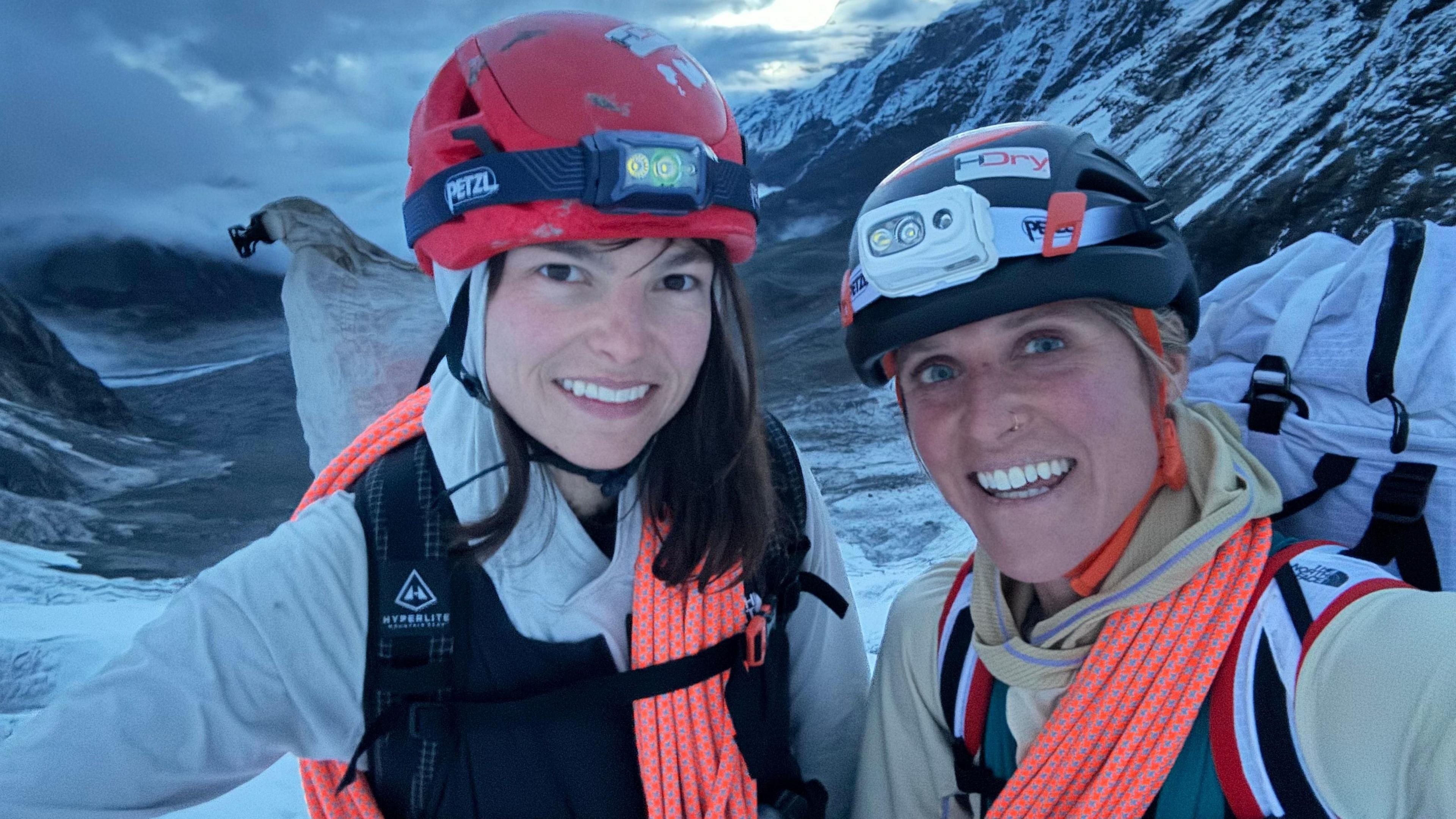 Fay Manners with her climbing partner Michelle Dvorak on a snowy mountain top. They are wearing helmets and smiling at the camera.