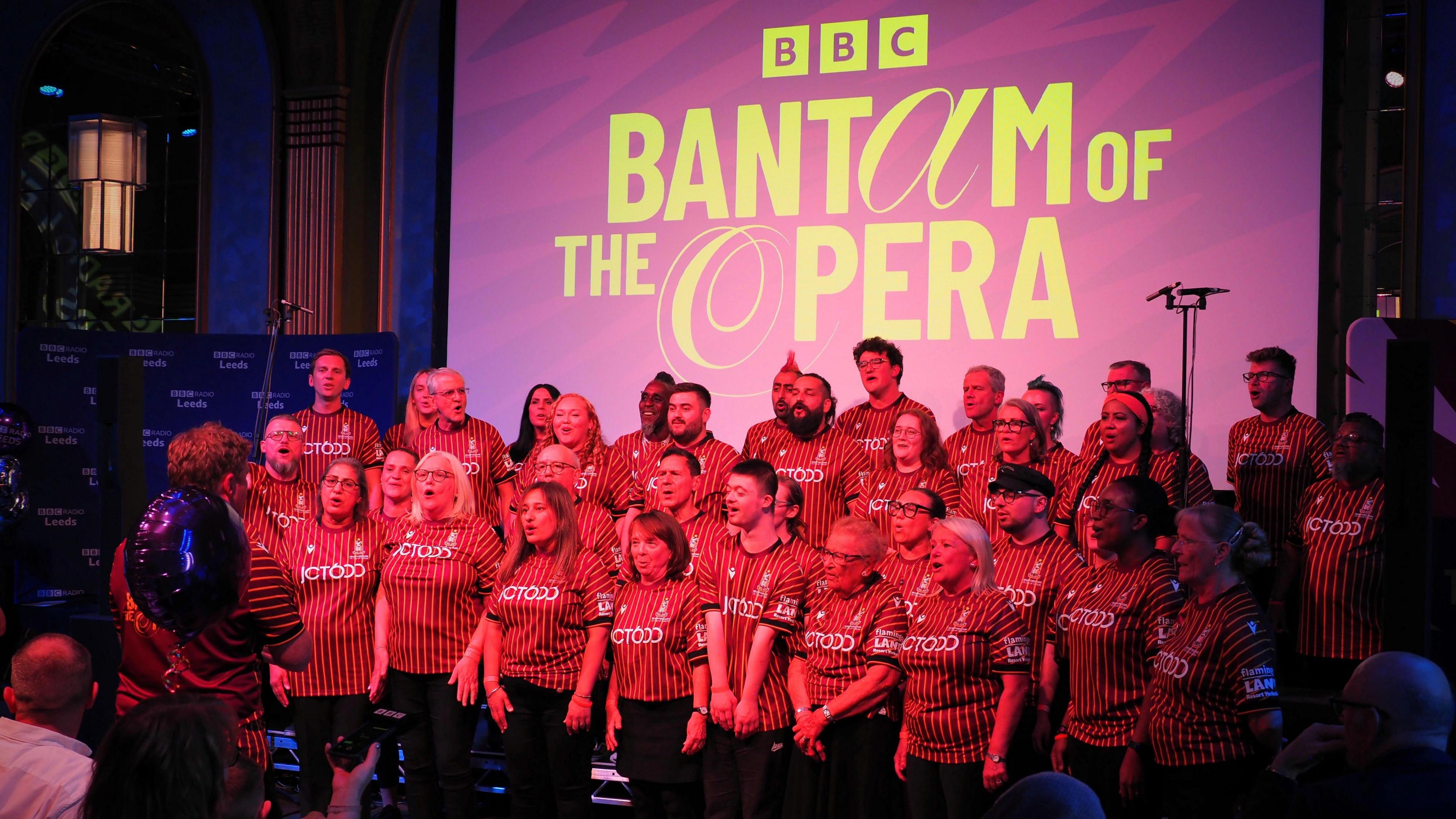 People wearing Bradford City tops singing in a choir. A large purple sign behind them reads: "BBC Bantam of the Opera."