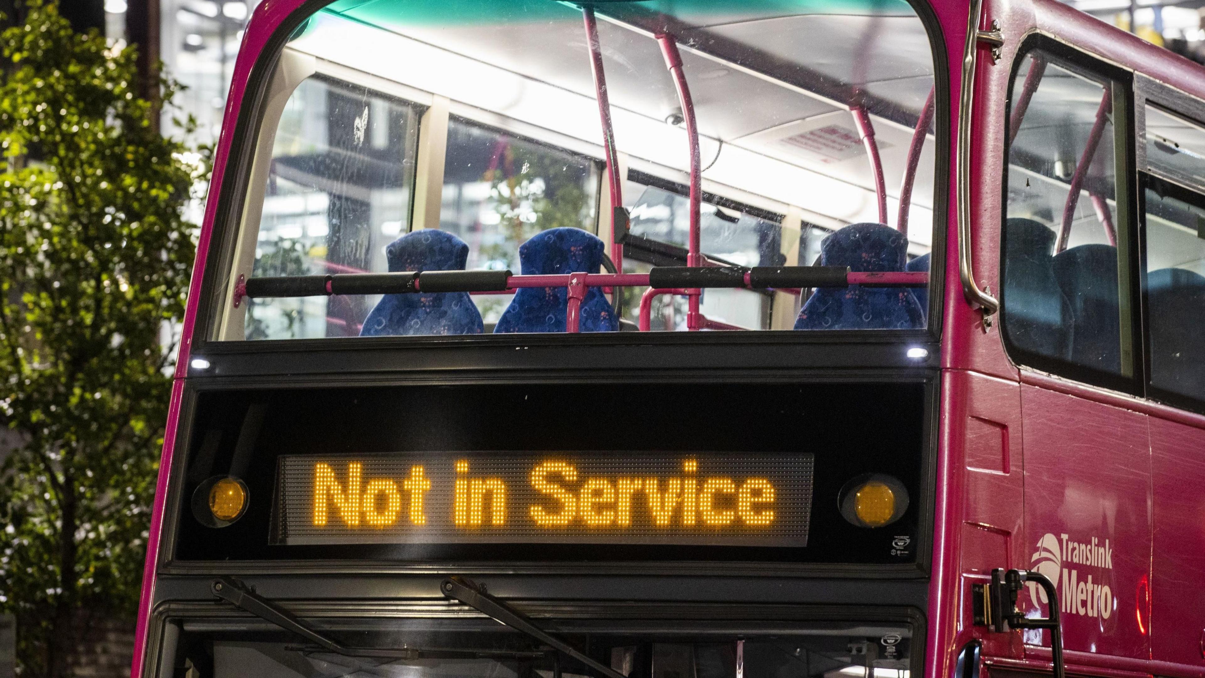 A pink Translink metro bus, on the front of it are the words not in service in yellow.