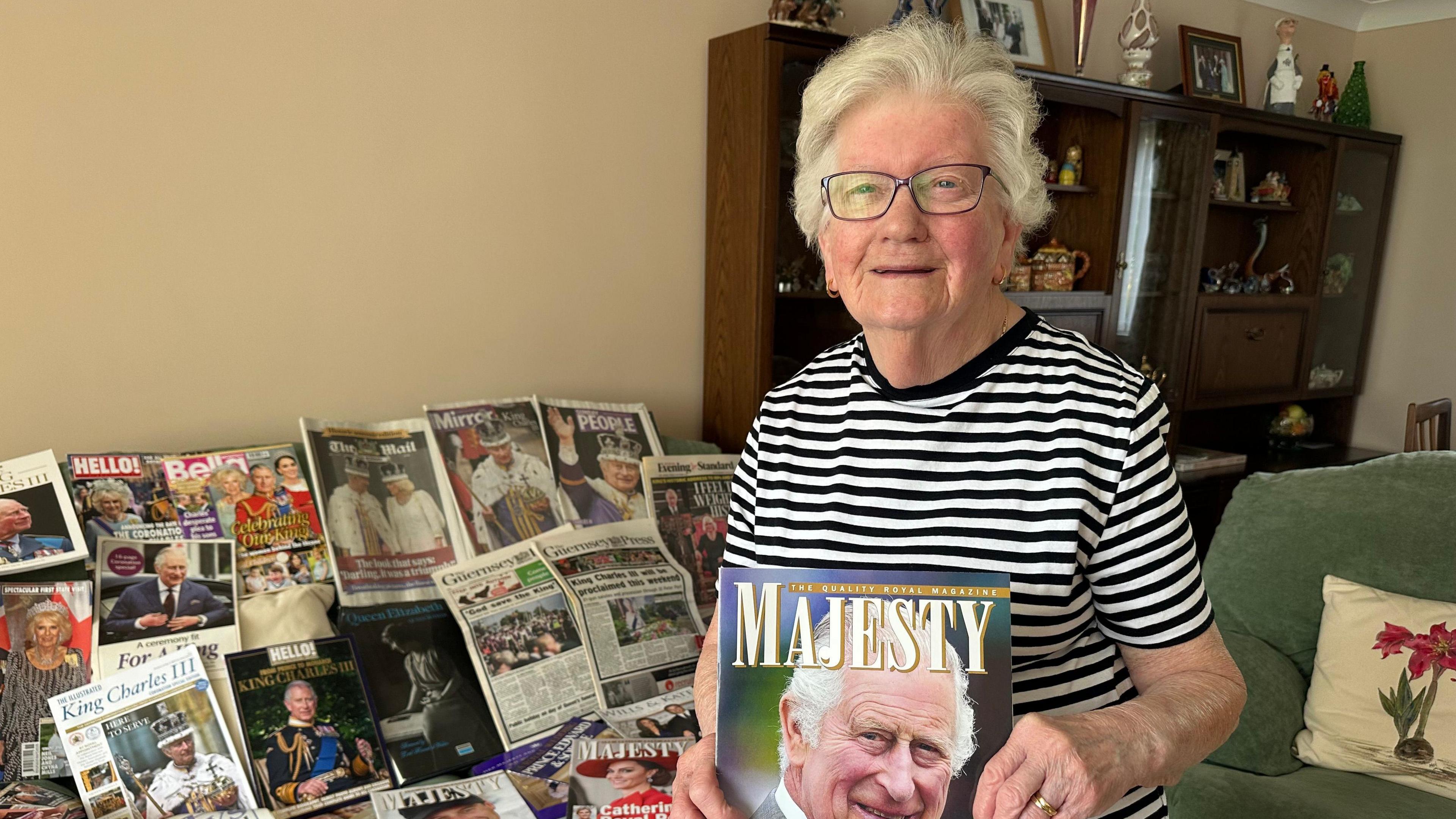 A woman holding a magazine with a picture of King Charles. Table with magazines and newspapers