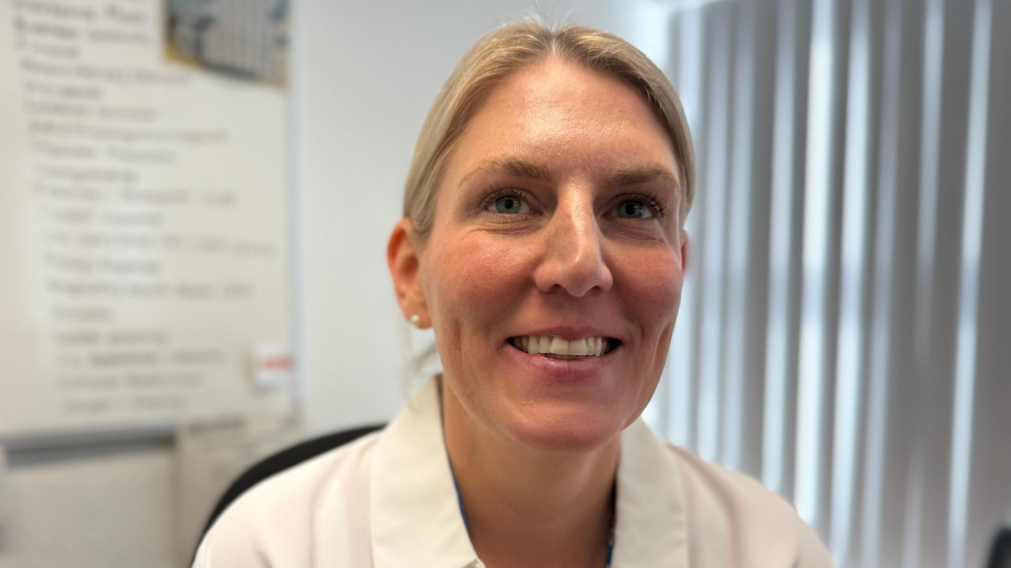 Victoria has blonde hair which is tied behind her head away from her face. She is wearing a white shirt. She is pictured at her desk on the hub. 