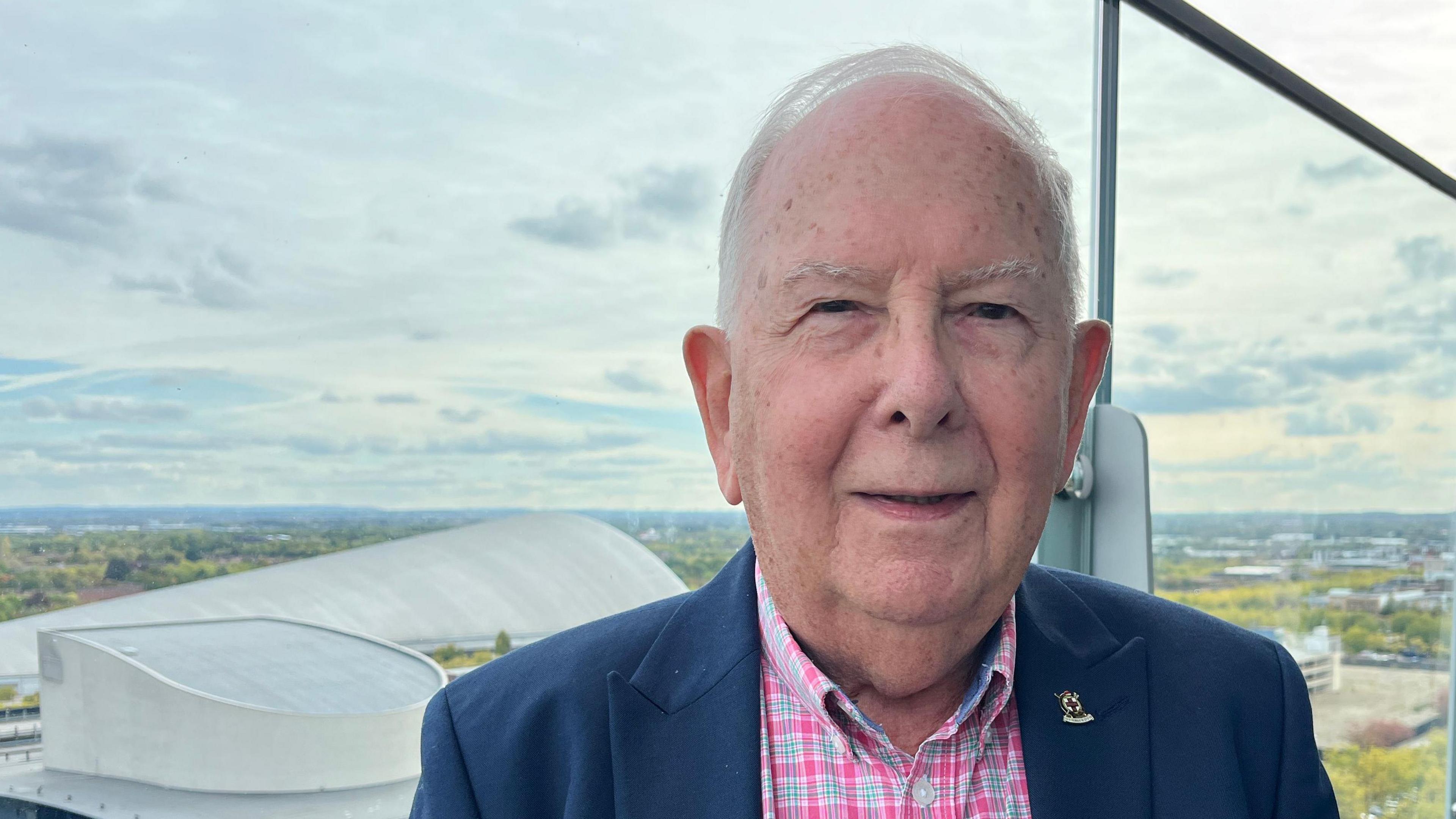 David Stabler from Central Milton Keynes Town Council. He is wearing a navy blazer over a pink shirt. He is smiling and looking into the camera. 
