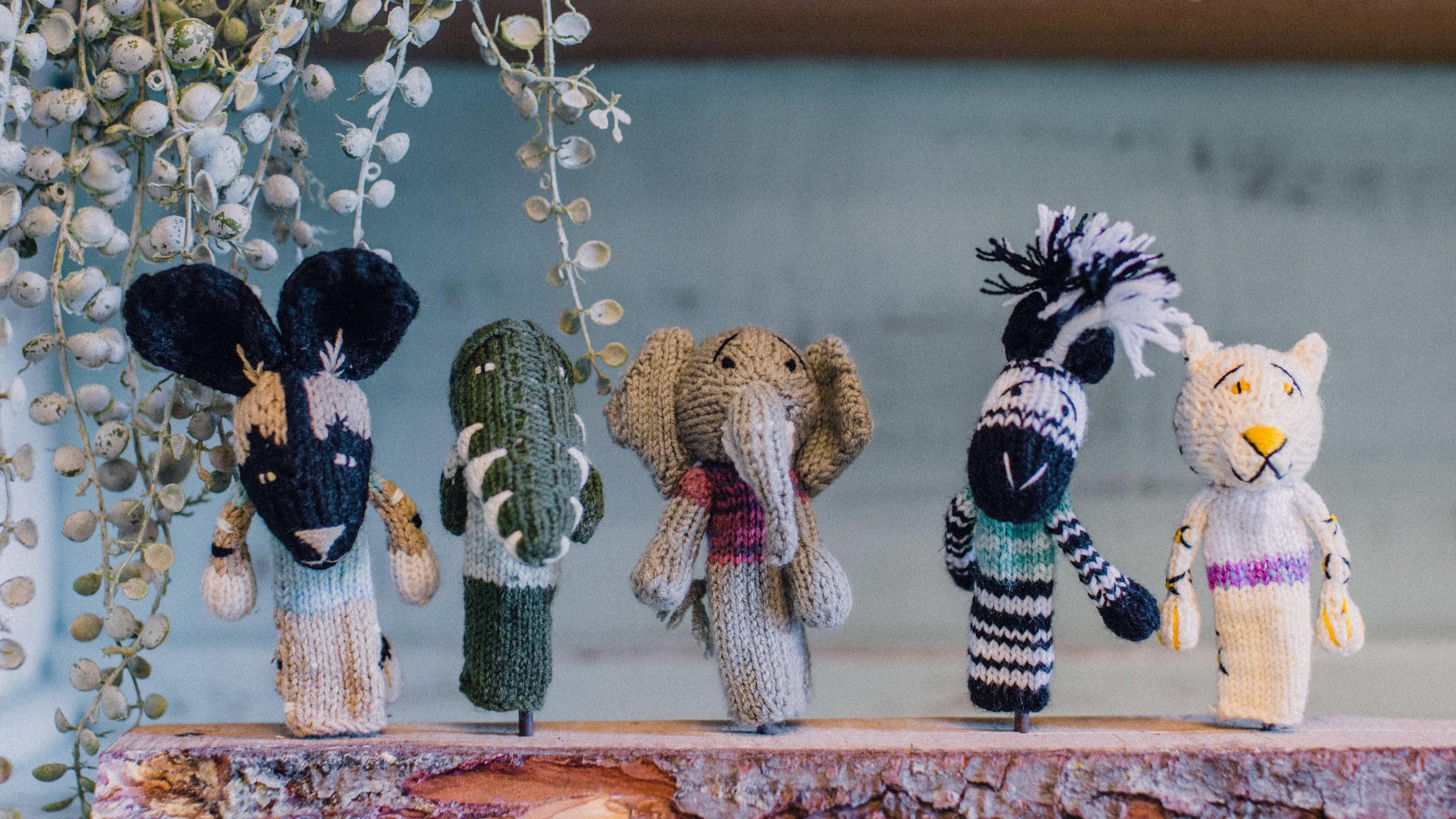 Five knitted finger puppets in the shape of various animals, displayed on a piece of wood.