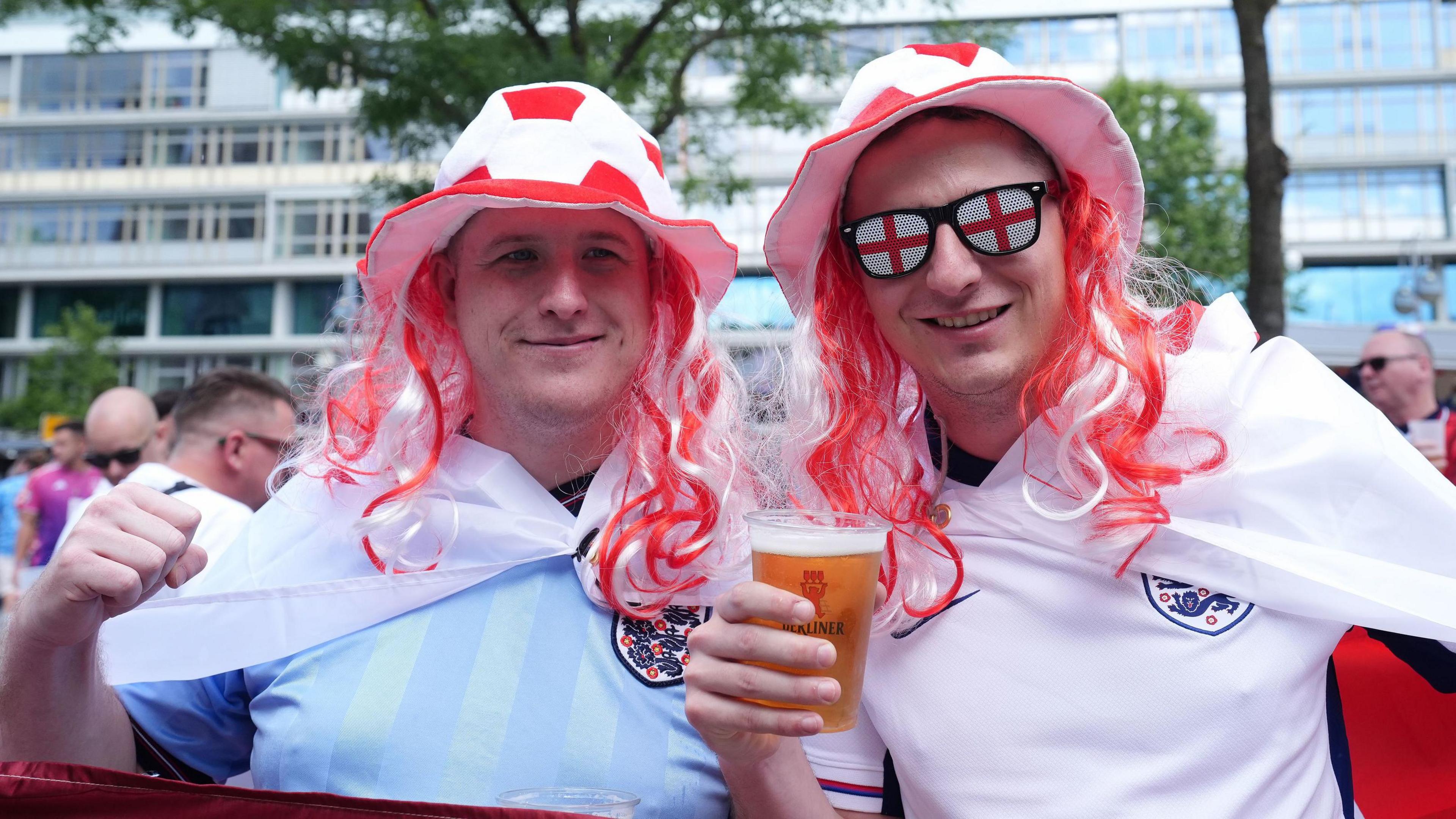 Two men wear England shirts and red and white hats with red and white hair attached to it