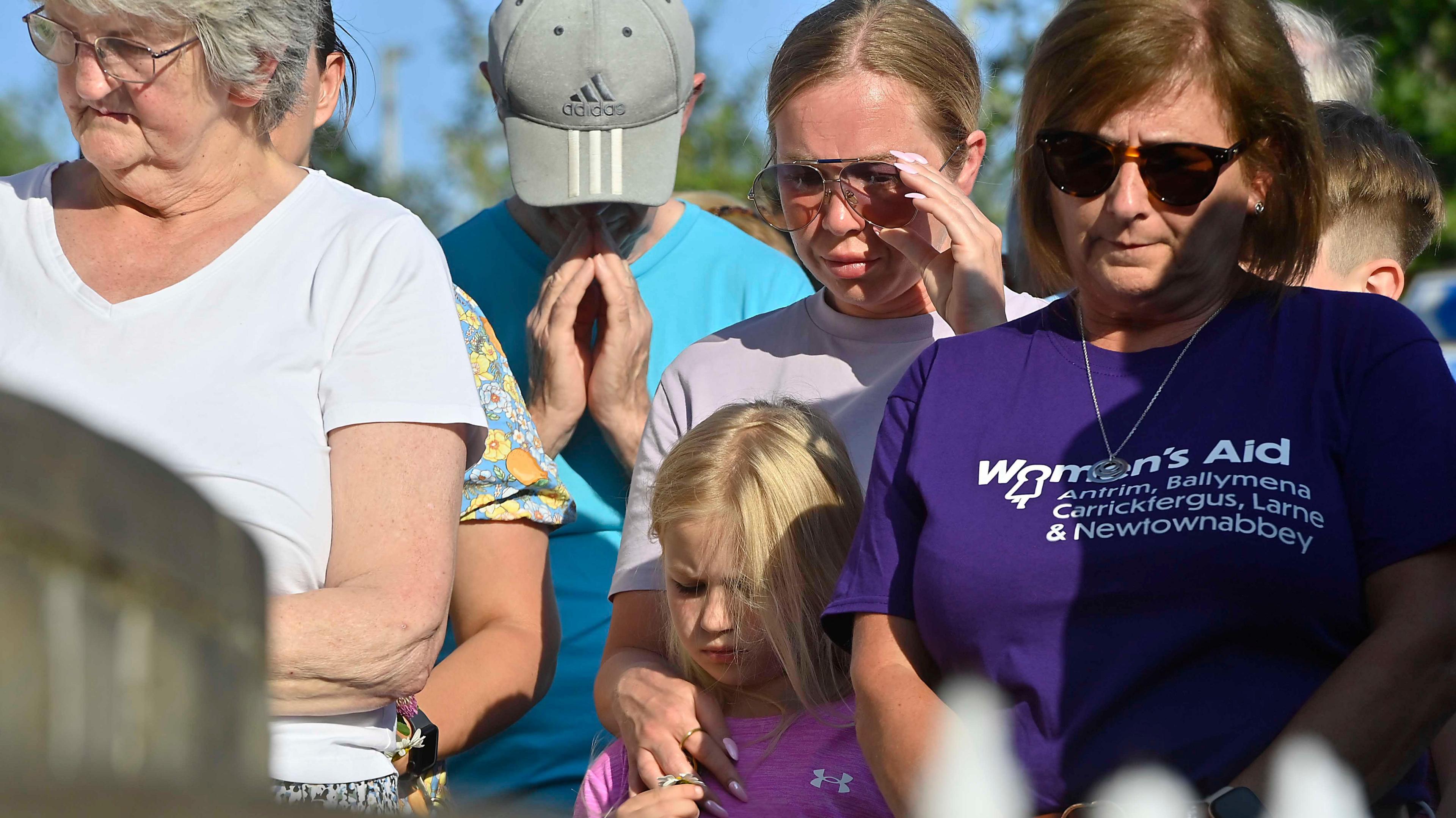 Three woman, a man and a little girl stand with their heads bowed as they paid tribute to the victims 