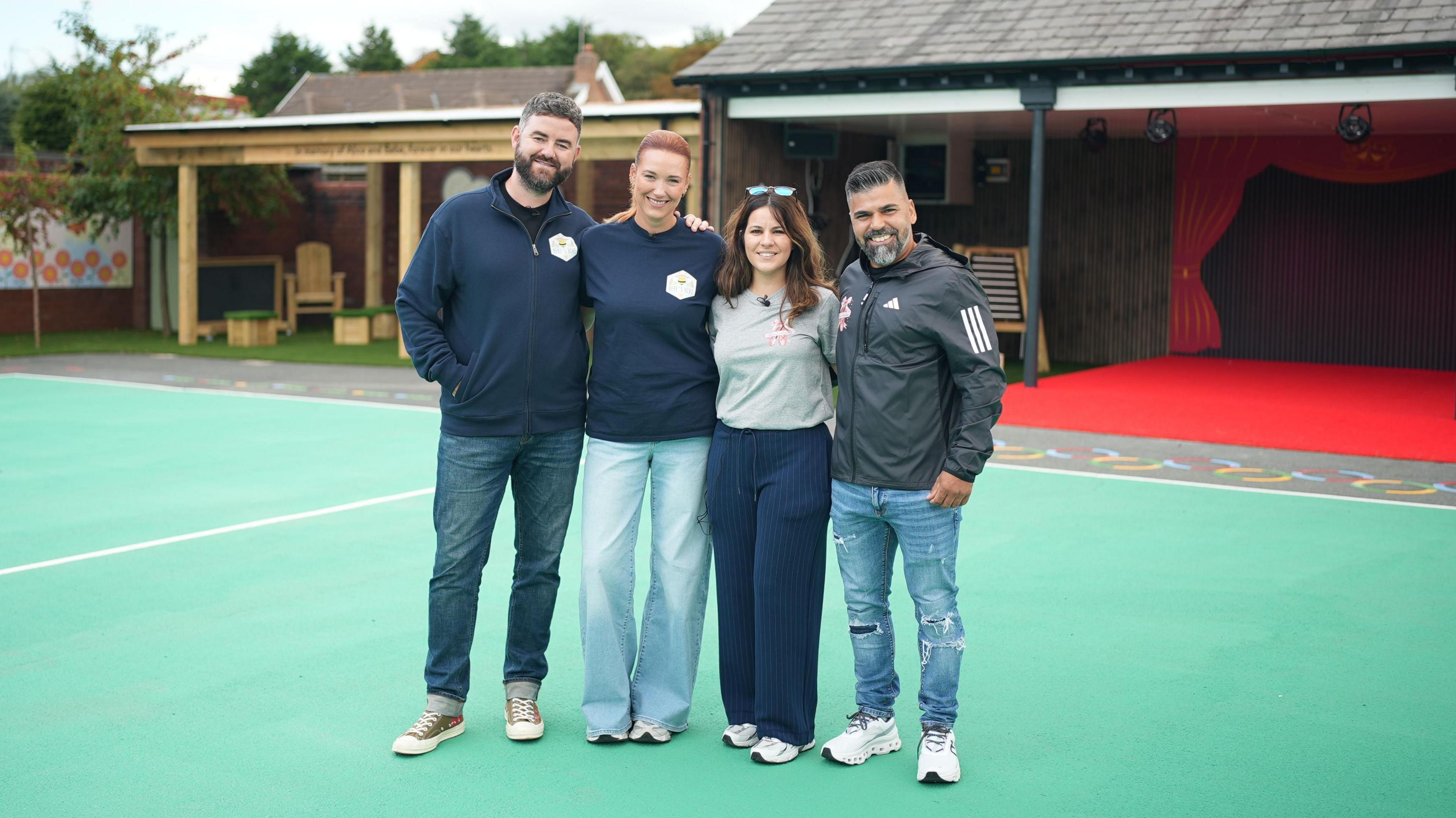 Ben King, Lauren King, Alexandra Aguiar and Sergio Aguiar stand in a row with their hands on each others' shoulders as they smile for a photo in the new playground.