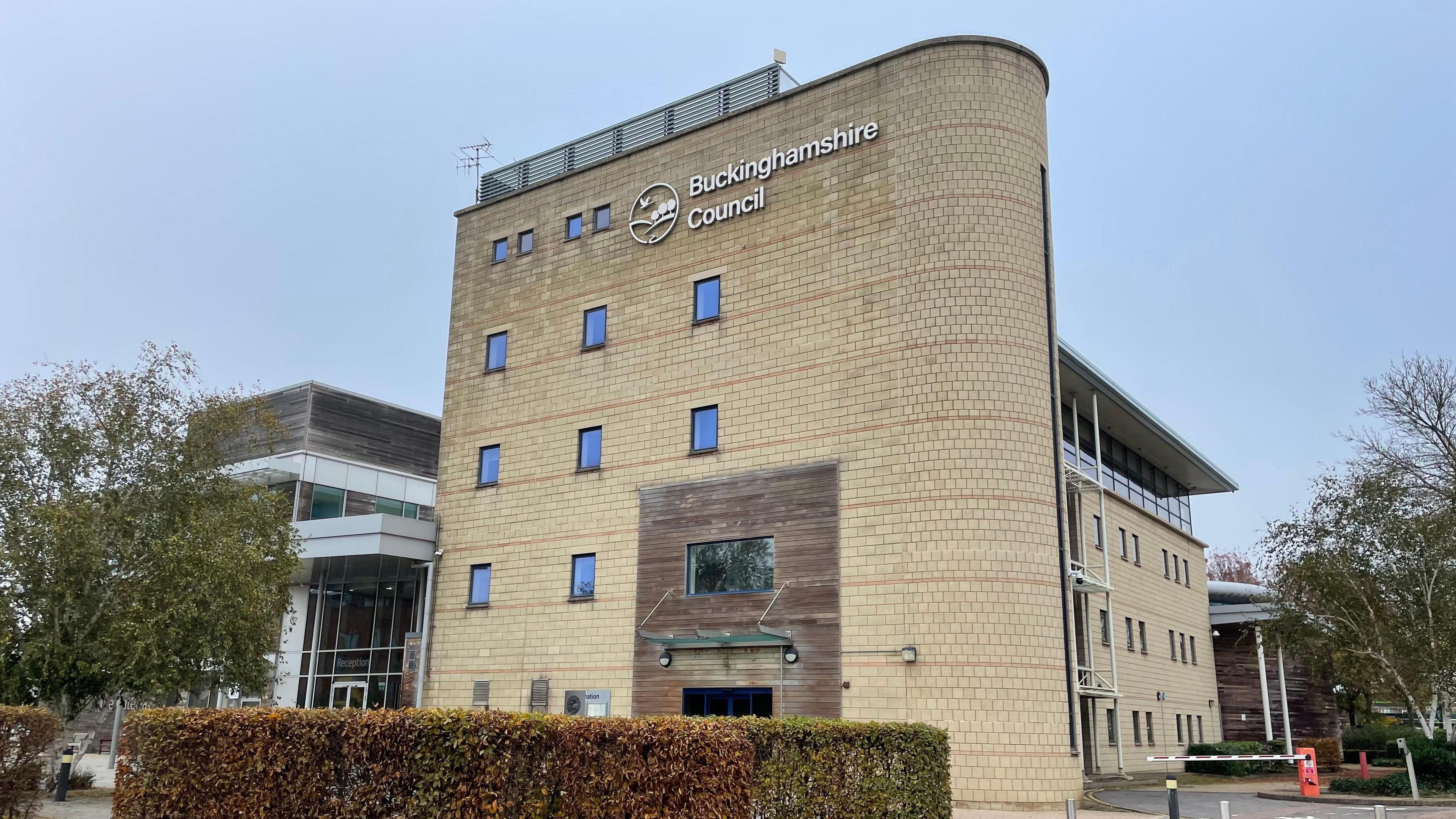 A view of Buckinghamshire Council's headquarters. The yellow brick building is several stories high and has windows on each floor.