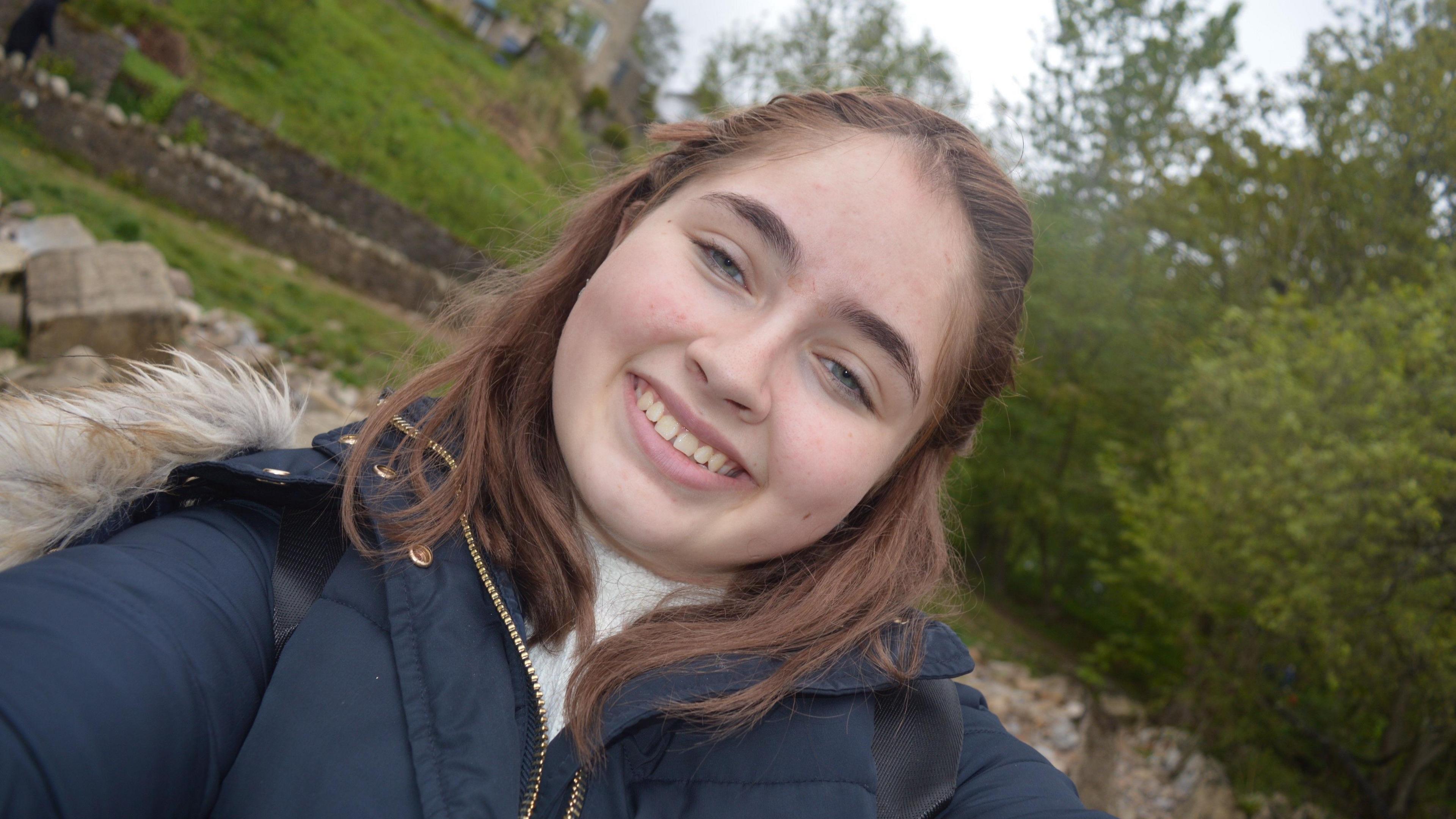 A young woman with long brown hair smiles into the camera.