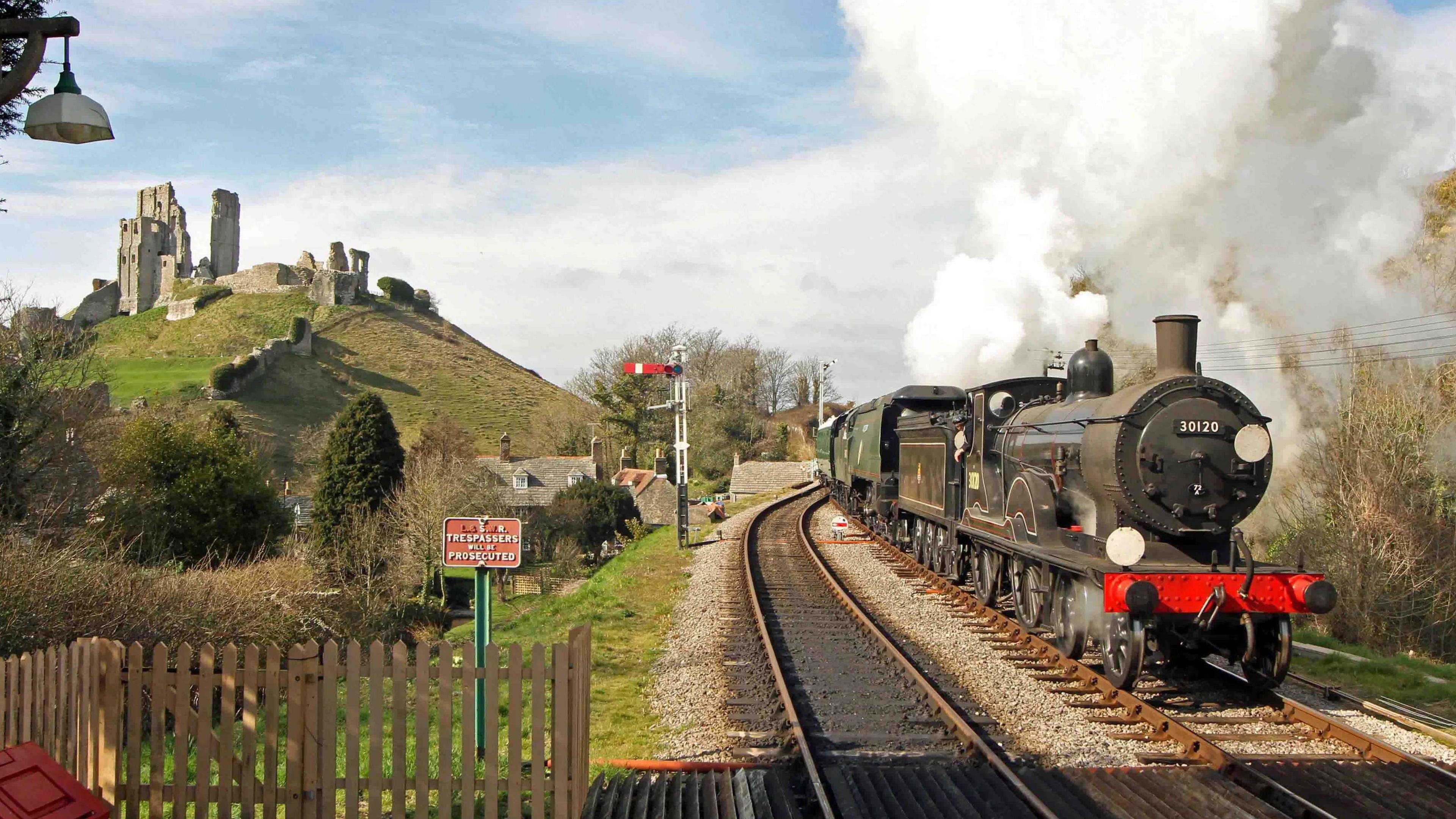 A black steam locomotive travelling past the ruins of Corfe Castle