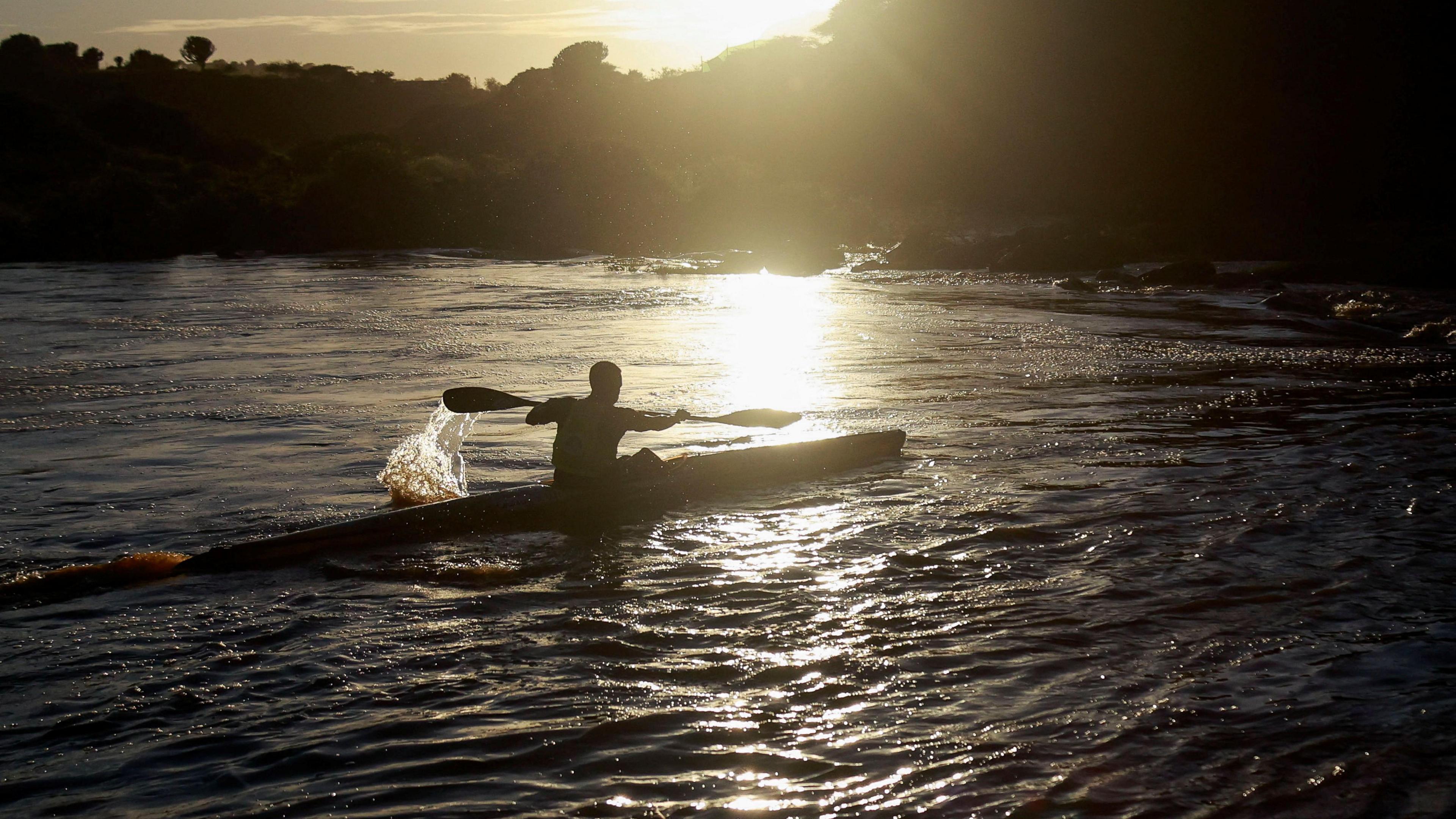 A silhouette of a paddler steering their canoe down a river as the sun sets behind them in  Ximba, South Africa, 21 February 2025.