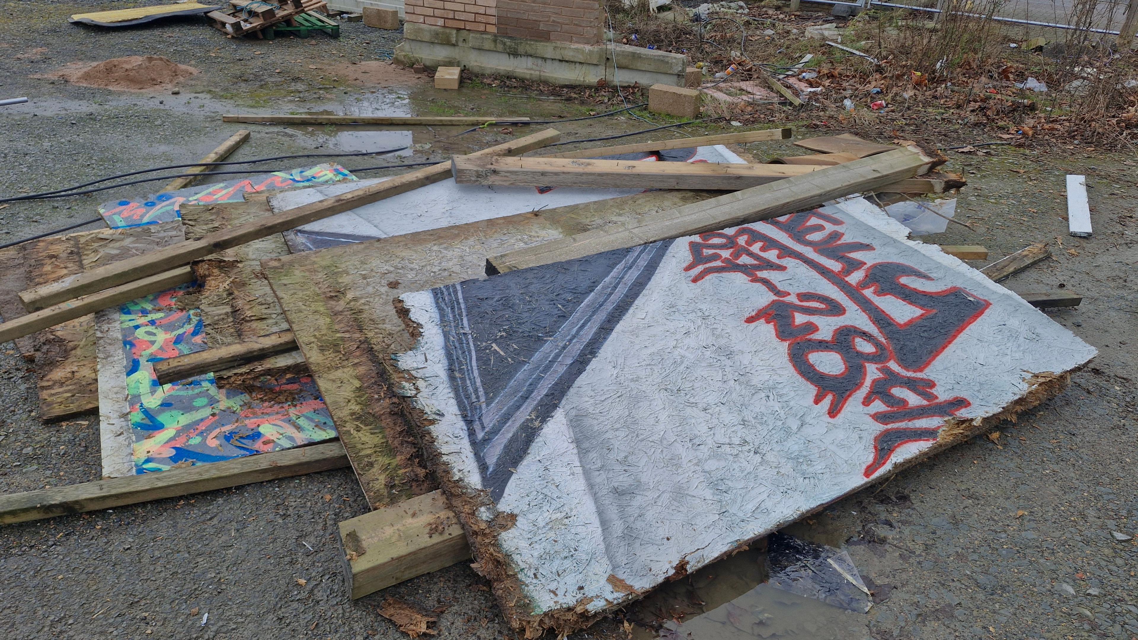 boards with artwork on them lying on barren wasteground with a brick wall in the background