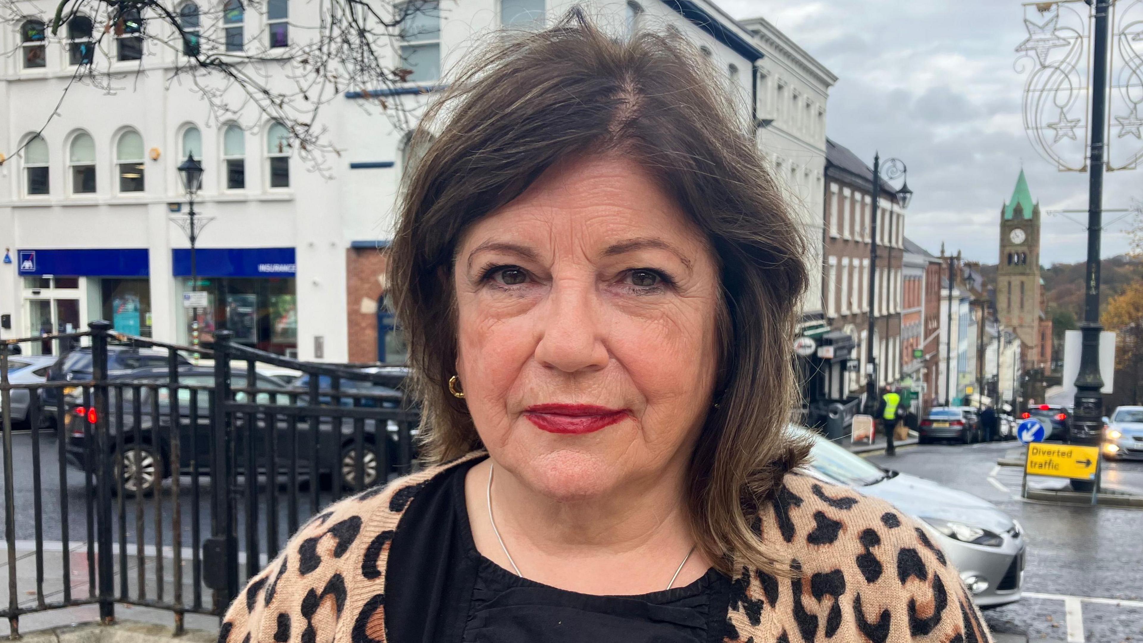 Marie Brown has long brown hair and is wearing a leopard print cardigan and black T-shirt. She is standing in Londonderry city centre.