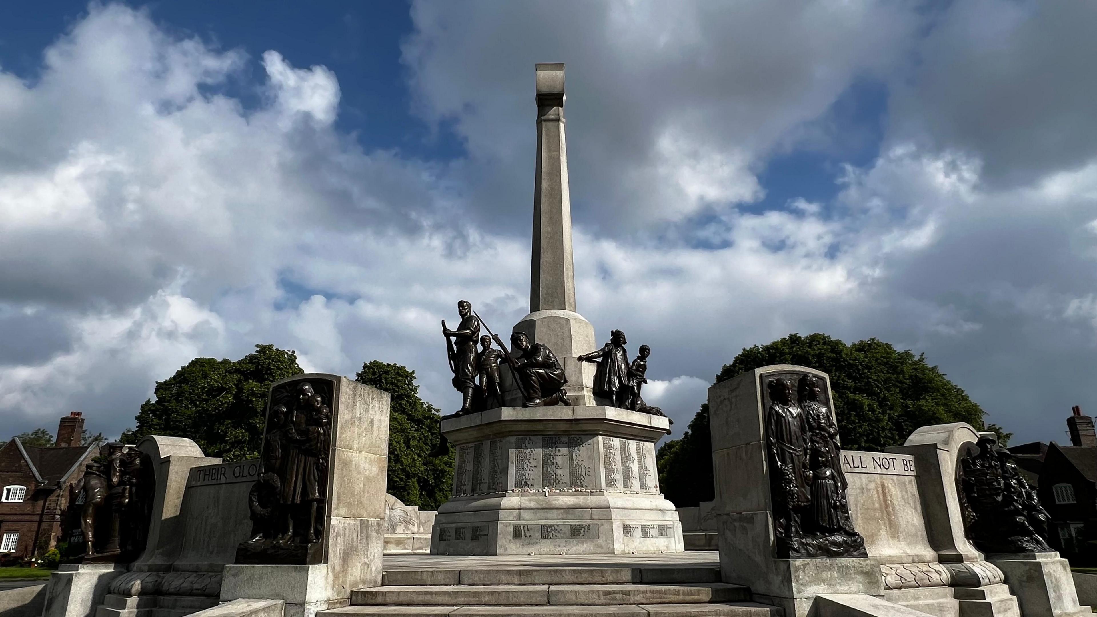 War memorial with statues depicting soldiers. Engravings of names of the fallen just visible on the memorial with sky filled with cumulus cloud