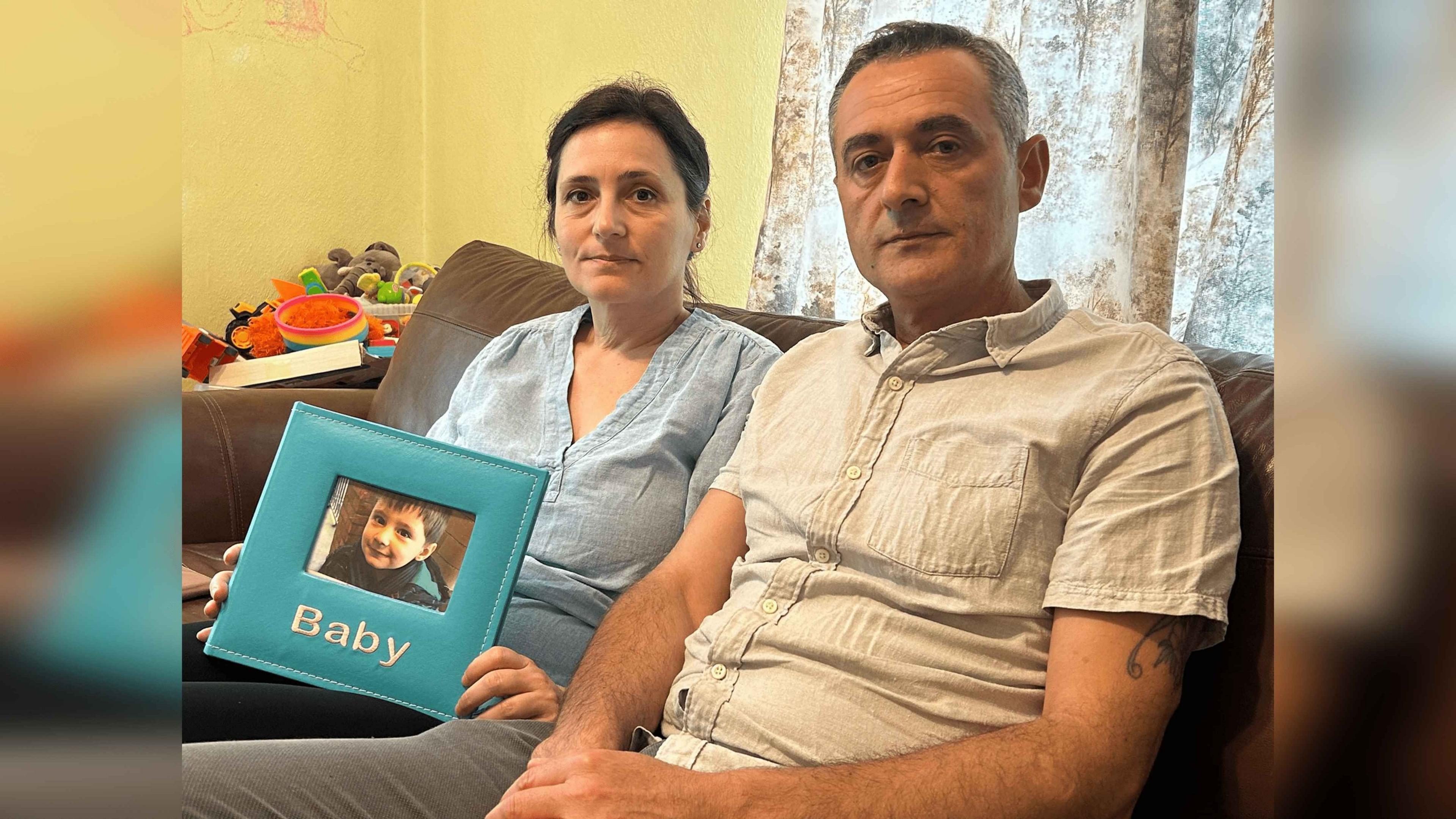 Lindita Alushi and Kastriot Klosi sit on a sofa holding a photo of Daniel