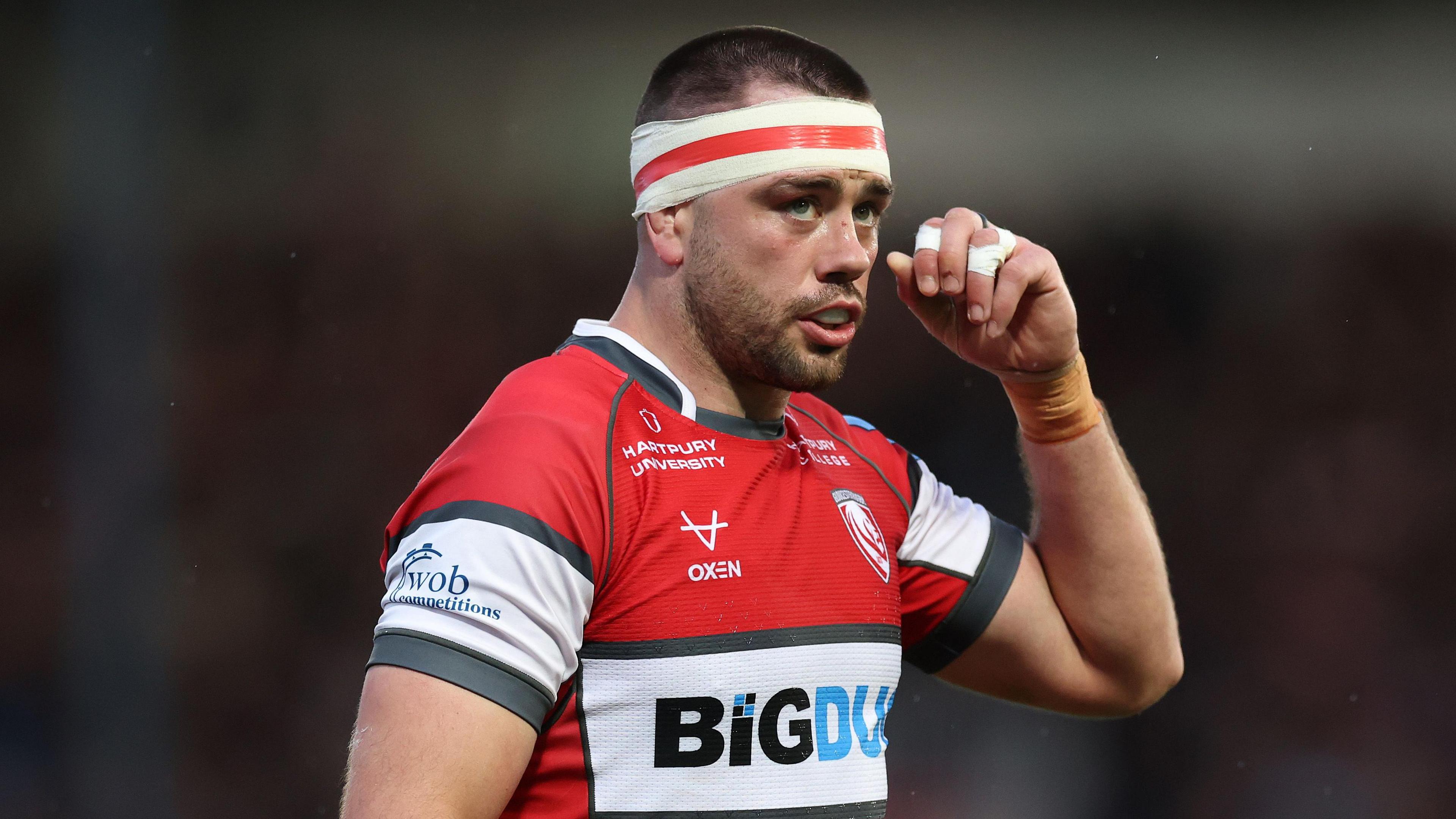 Lewis Ludlow holds his hand up to his face while standing on the pitch during a match for Gloucester
