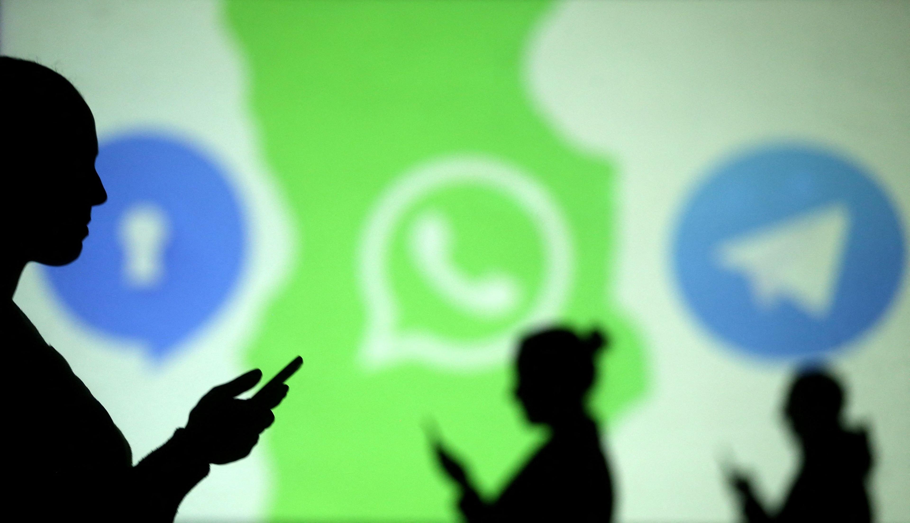 Silhouettes of mobile users are seen next to logos of social media apps 